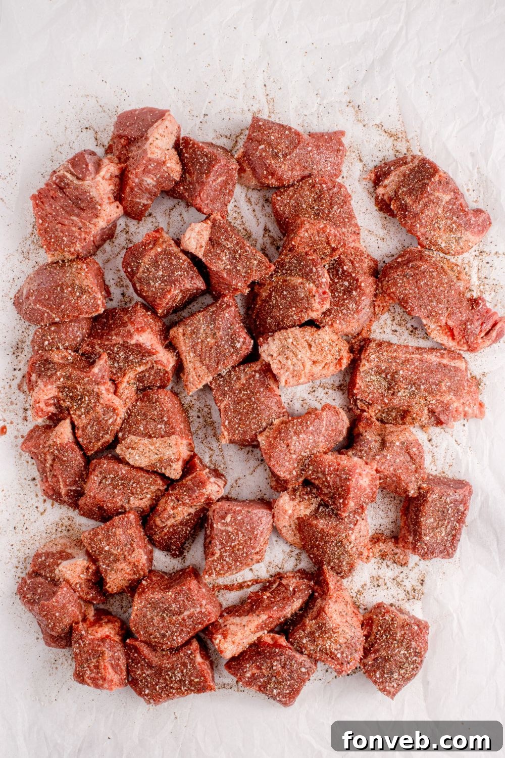 Beef chuck roast, expertly cut into uniform cubes, has been generously seasoned with a rich spice rub, ready for the smoker.