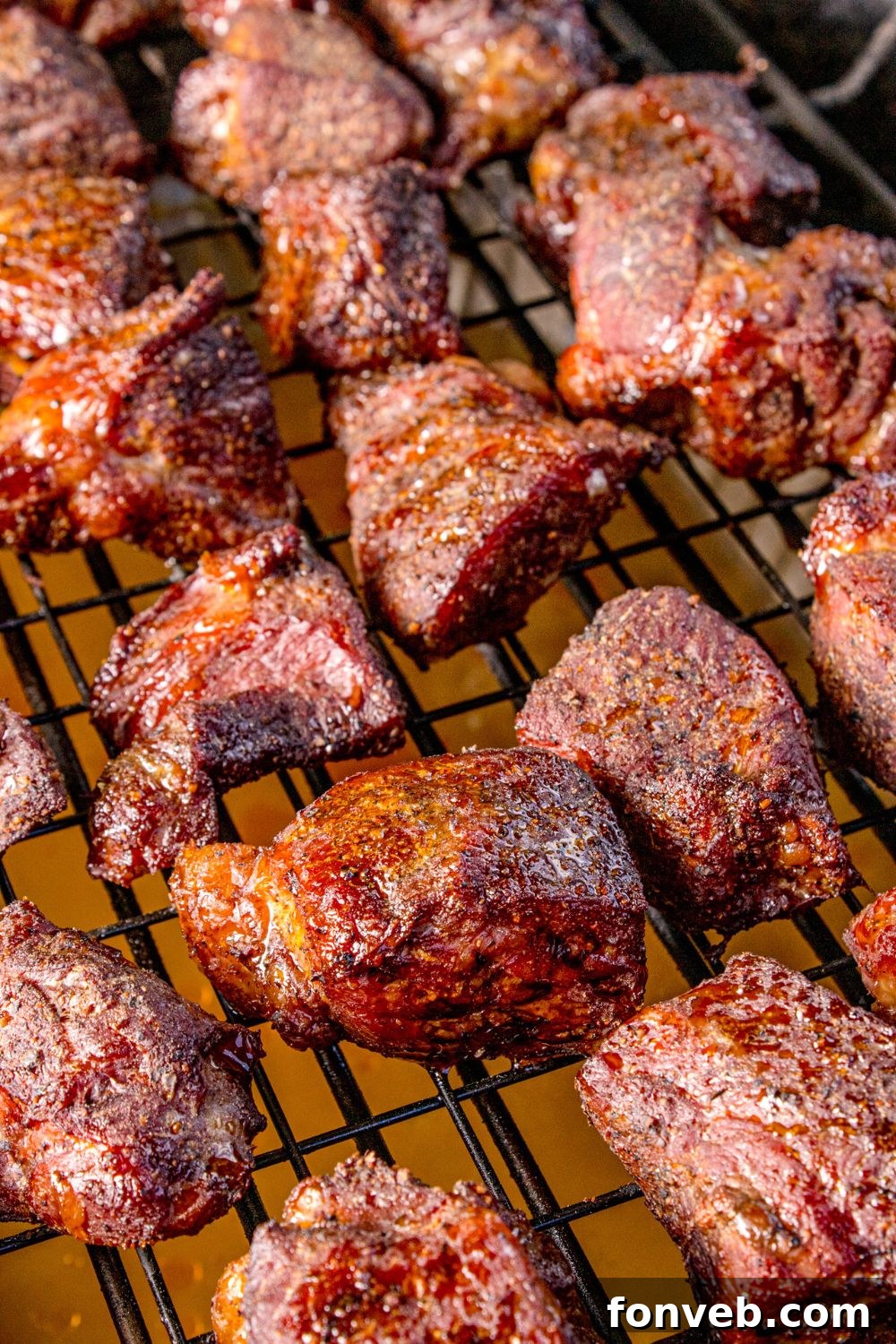A close-up view of beef chuck roast cubes cooking on a grill, showing the formation of a delicious, smoky bark.