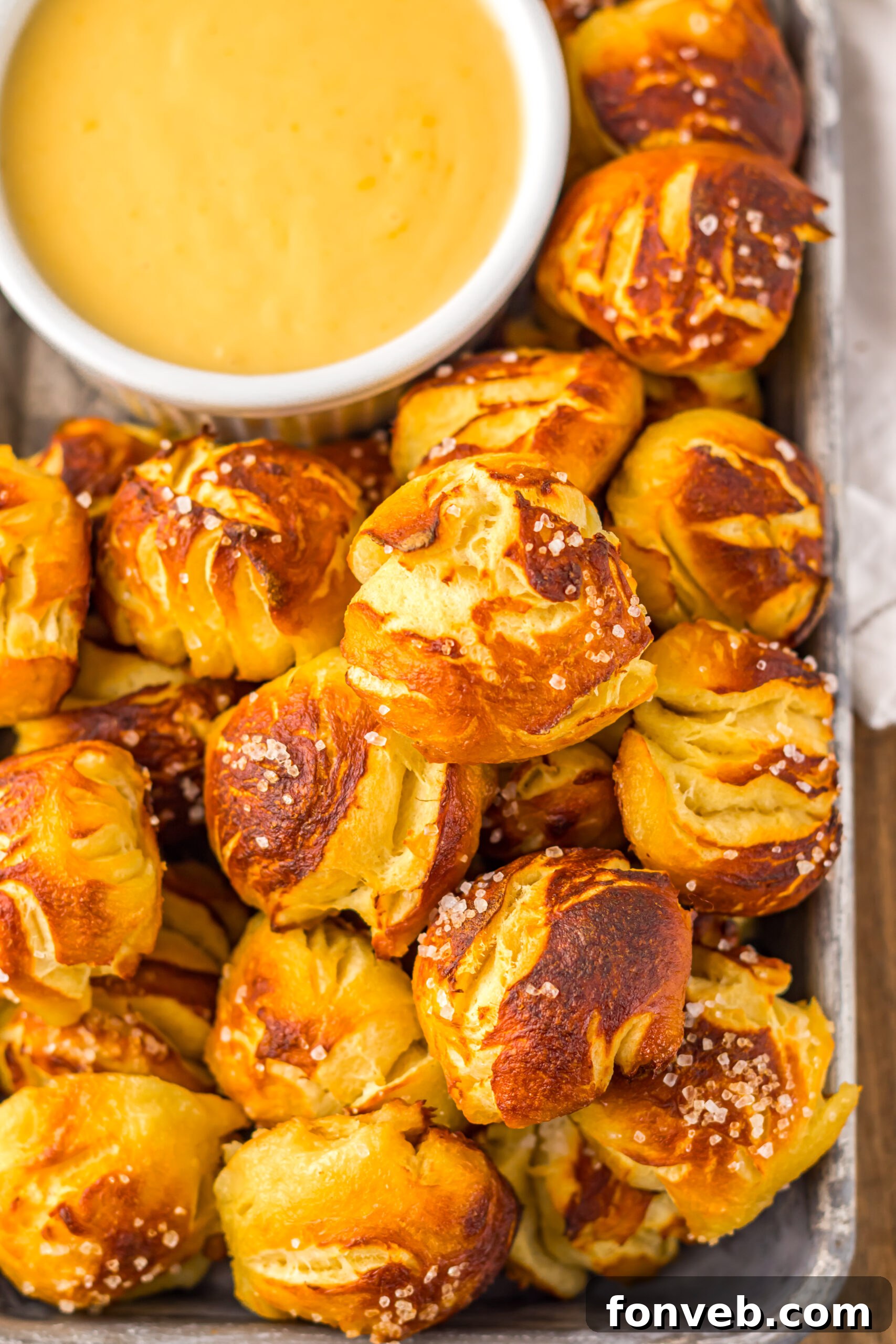 Easy Biscuit Pretzel Bites with Cheese Sauce on a tray sitting on table with a glass to the side 
