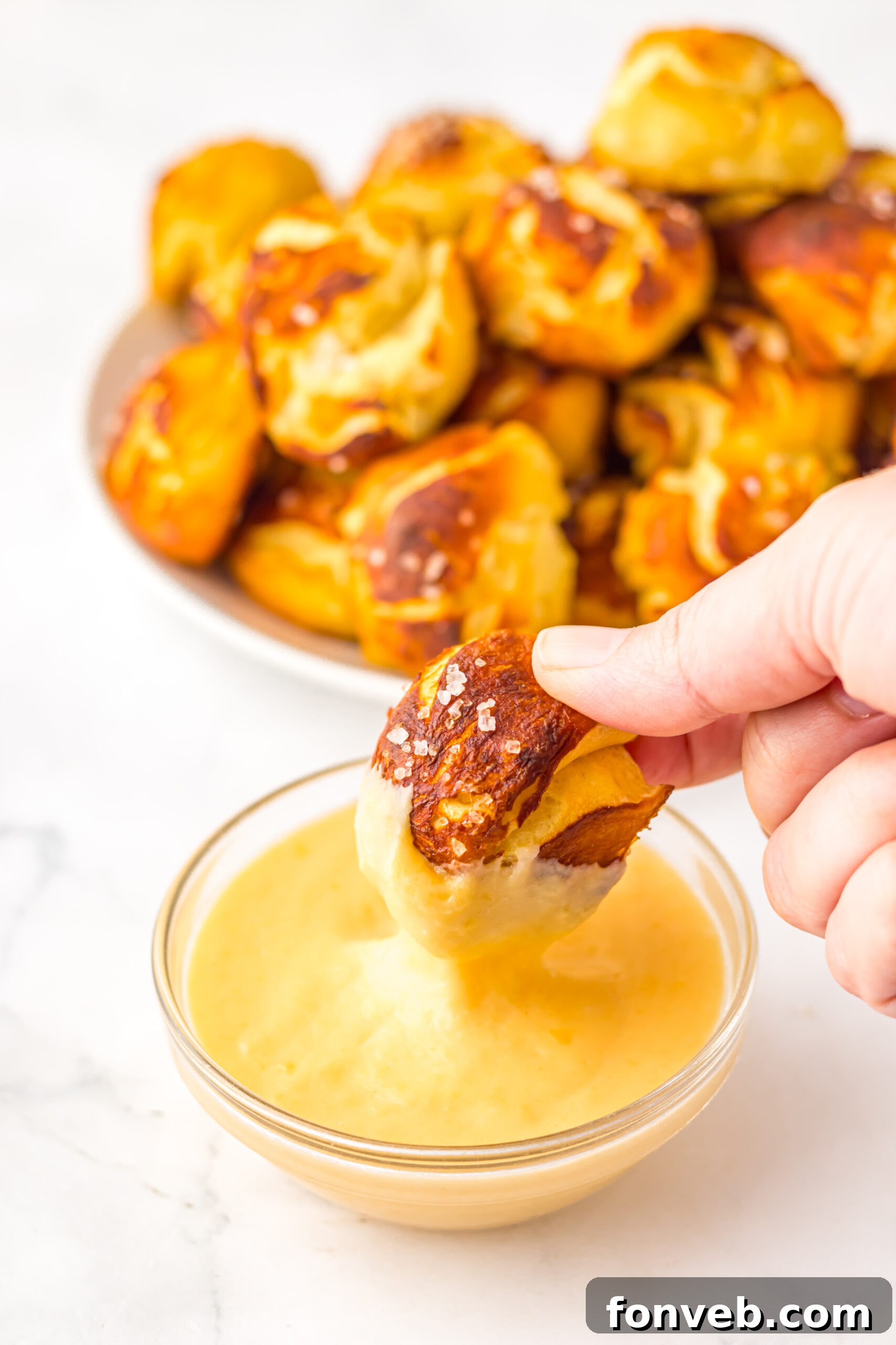 Easy Biscuit Pretzel Bites with a hand dipping one into the Cheese Sauce 
