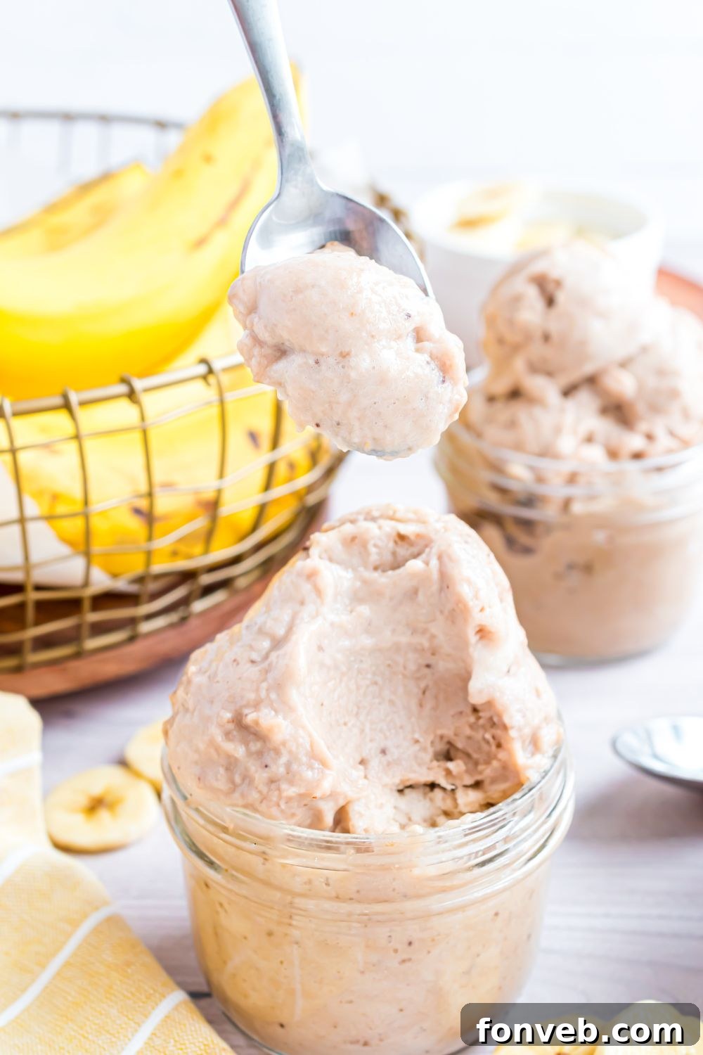 Banana Ice Cream: The One-Ingredient Wonder 21 Banana Ice Cream in jars on table with sliced banana to side and a bowl of bananas behind it on table