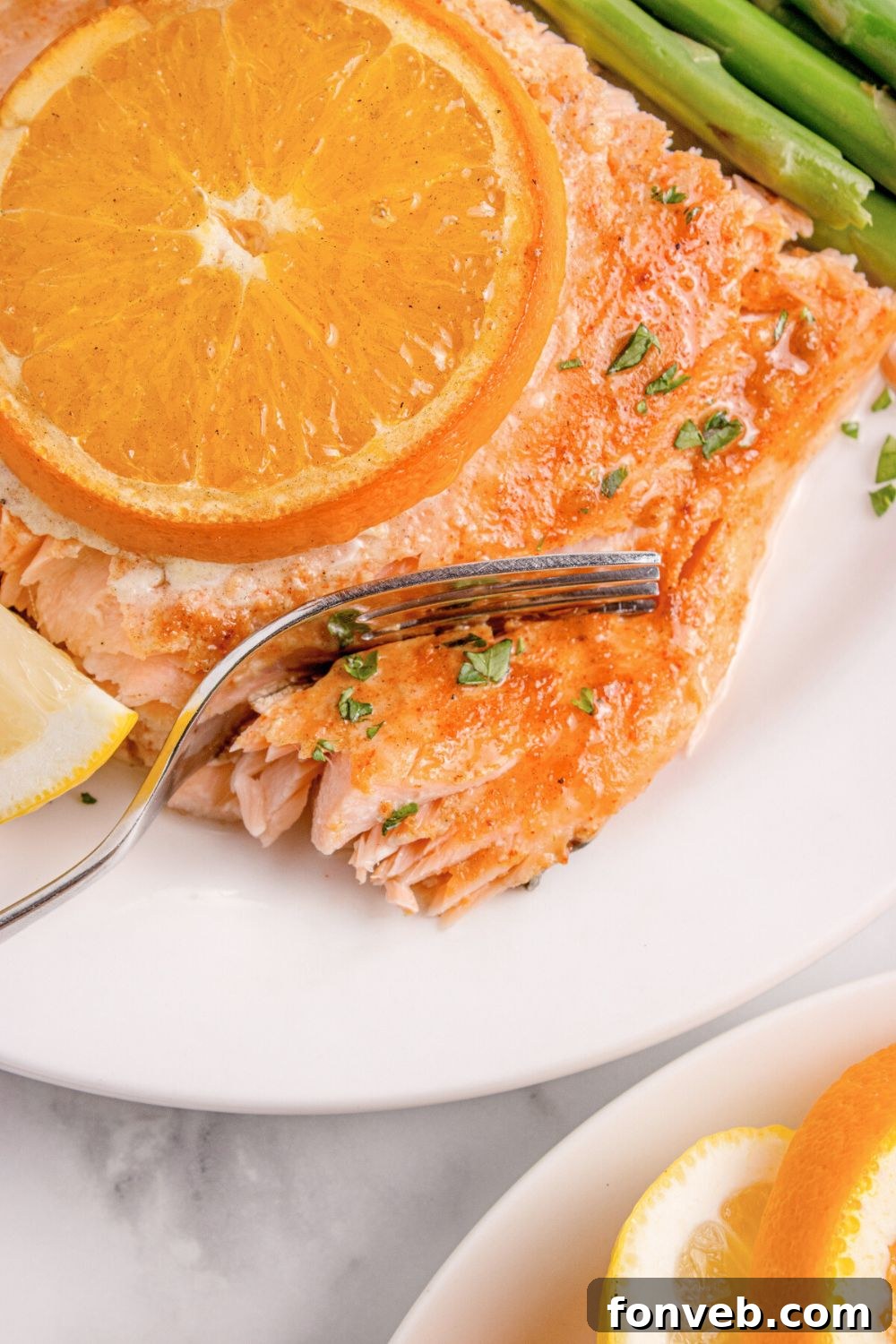 Effortless Honey Mustard Salmon Foil Grill 16 salmon on plate with an orange on top, with a fork cutting into the salmon, and asparagus to side