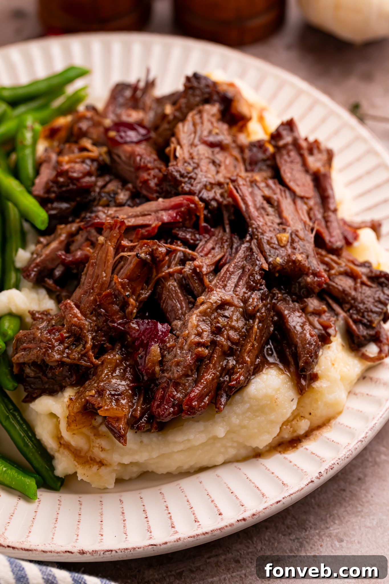 Cranberry Pot Roast shredded on a white plate with mashed potatoes under and a side of green beans 