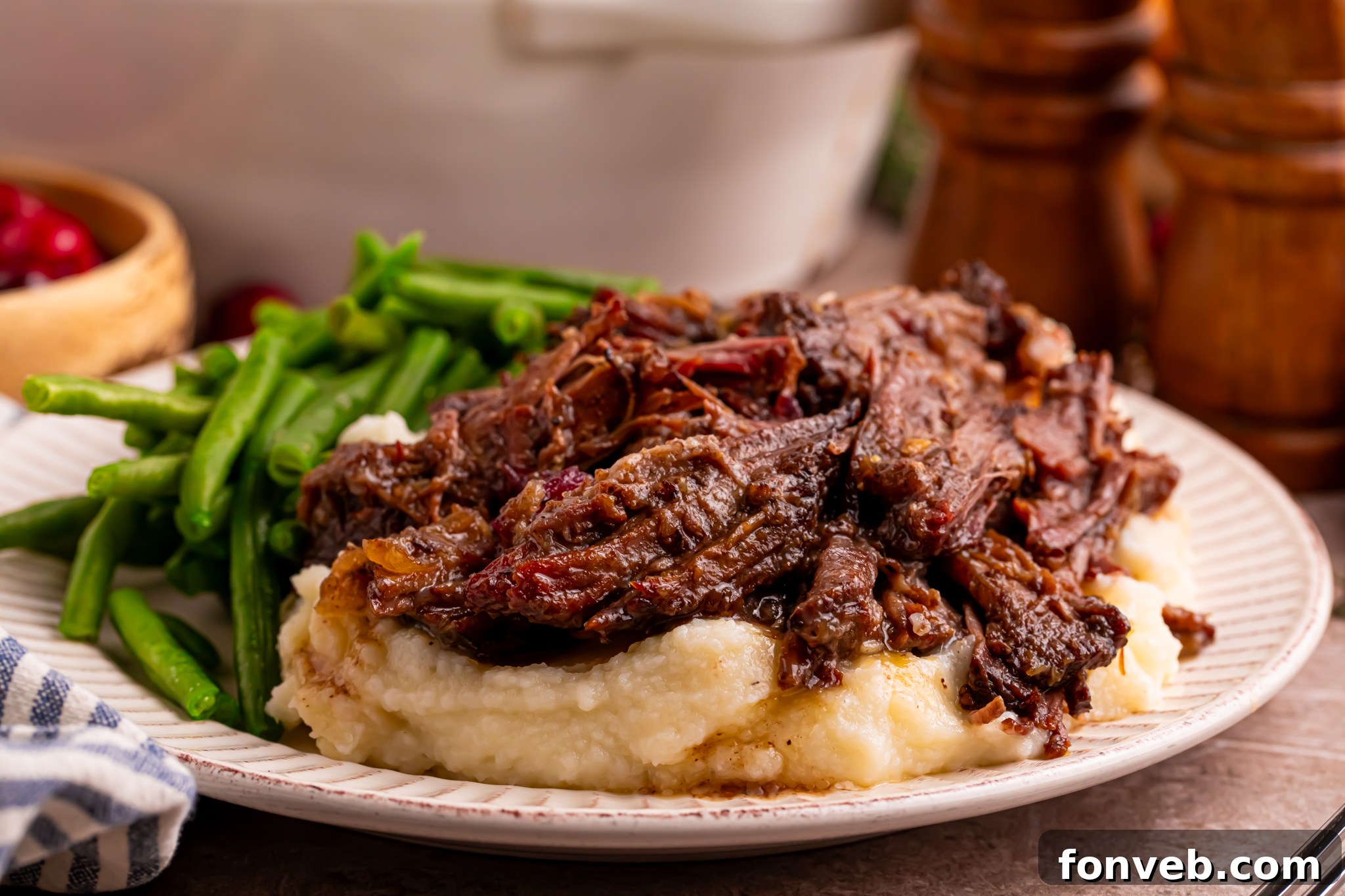 Side view of the Cranberry Pot Roast shredded on a white plate with mashed potatoes under and a side of green beans 