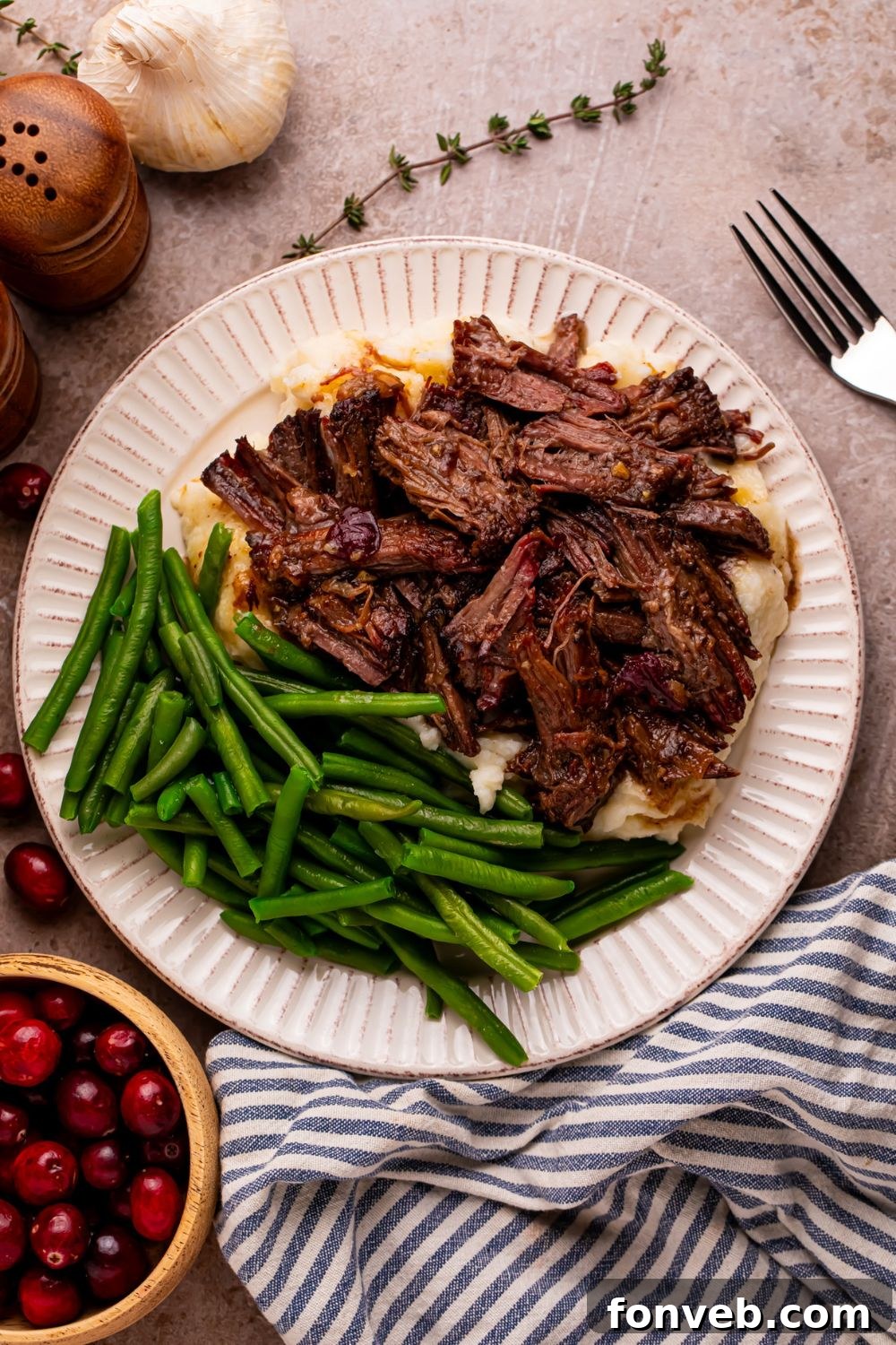 overhead look of plate with Cranberry Pot Roast and green beans. A bowl of cranberries to side of plate on table 
