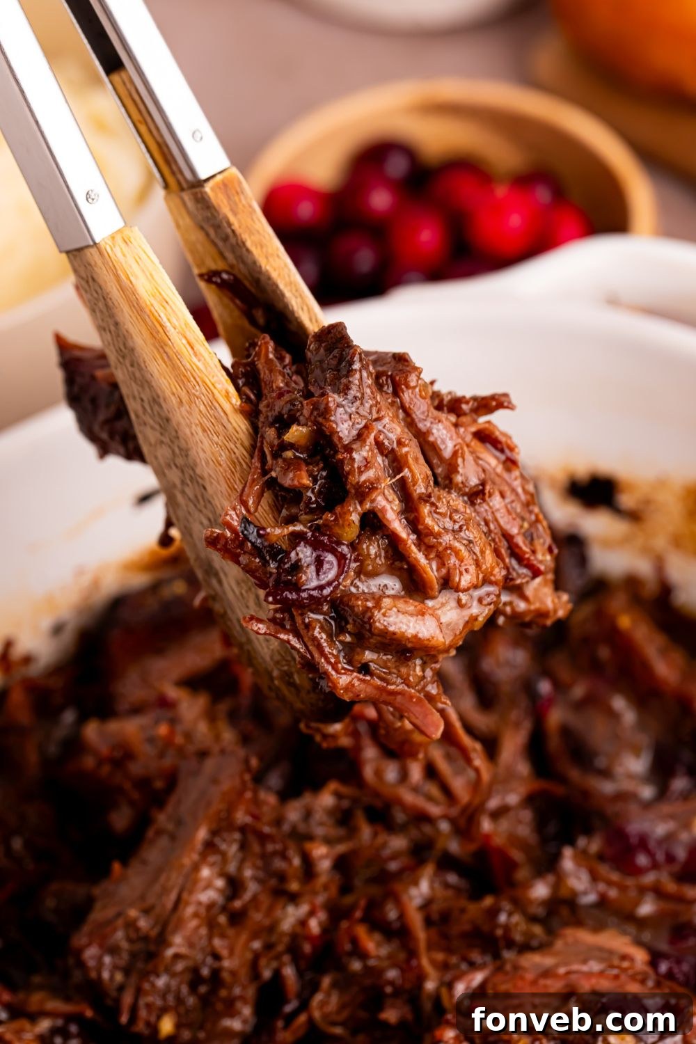 Cranberry Pot Roast in a pan and tongs lifting up some of the meat 