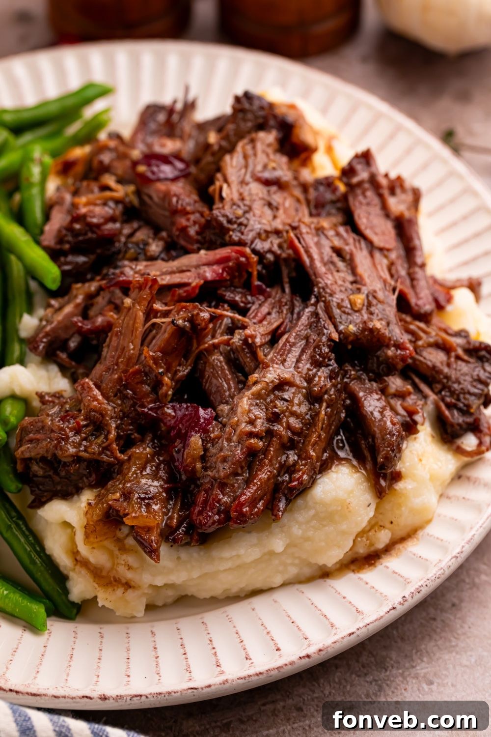 Cranberry Pot Roast shredded on plate with mashed potatoes under and a side of green beans 