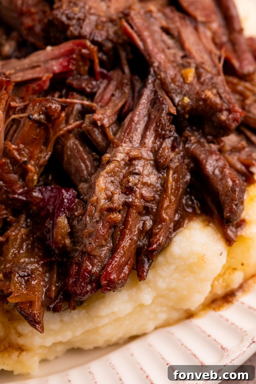Cranberry Pot Roast shredded and on plate with mashed potatoes under it 
