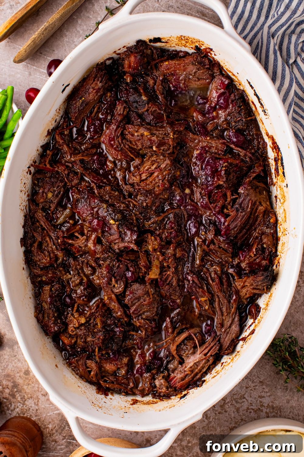 Cranberry Pot Roast shredded and in a pan on table with a towel to side of pan 