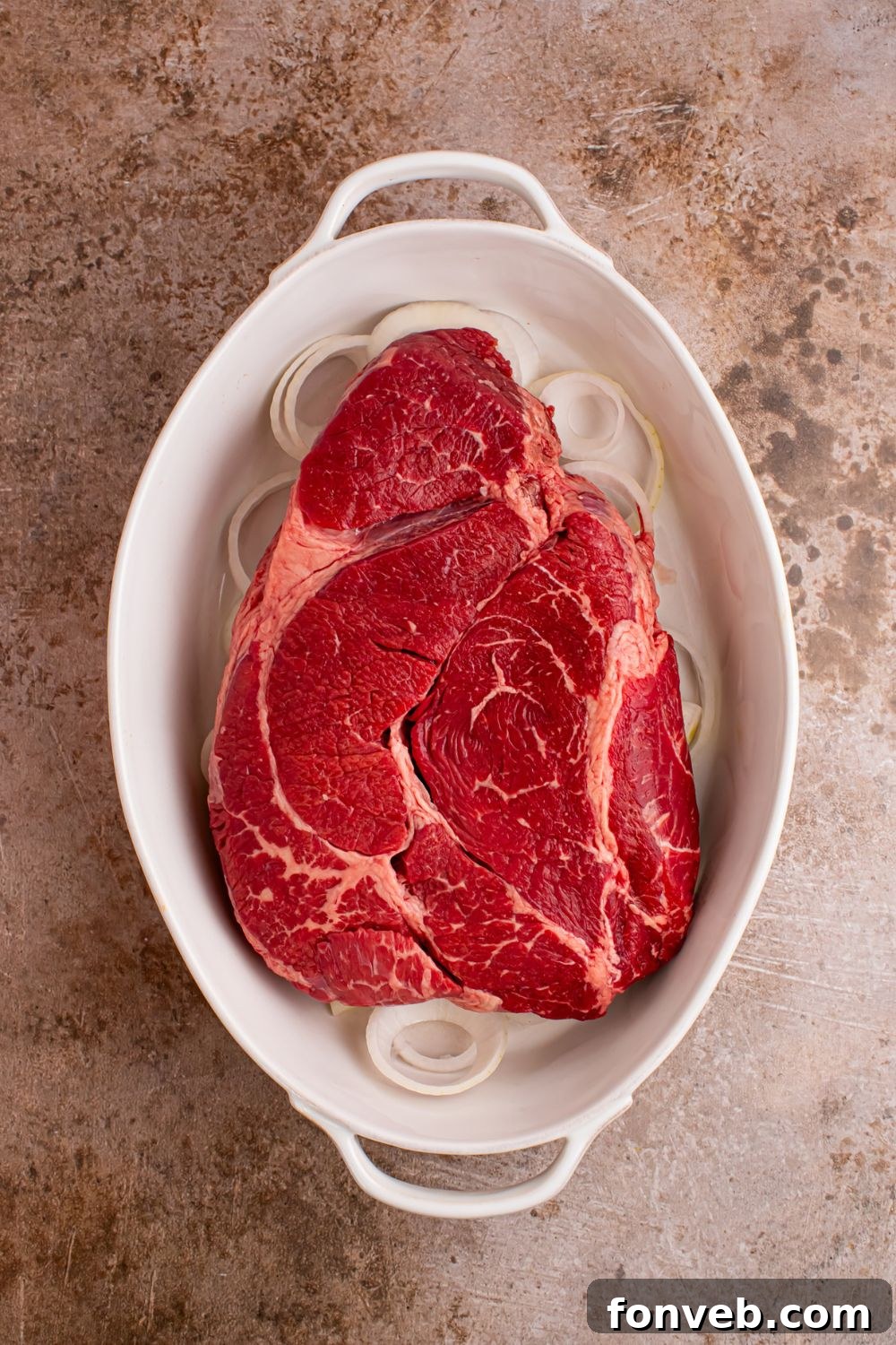 onion and raw pot roast in casserole dish on table 