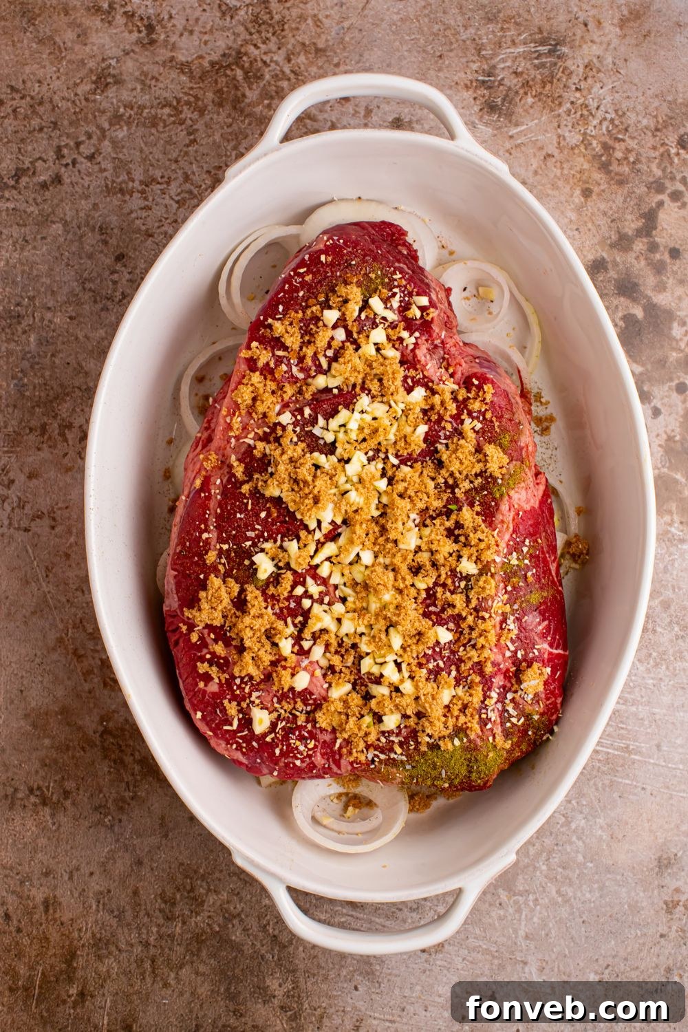 casserole dish with onions and pot roast on top with spices and seasonings 