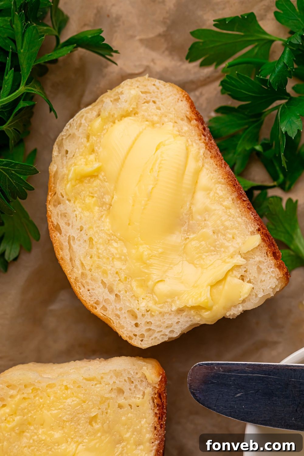 A 2-Ingredient Dinner Roll sliced in half, revealing its soft, airy interior, with butter and fresh herbs delicately placed beside it on a wooden table, emphasizing its delicious potential.