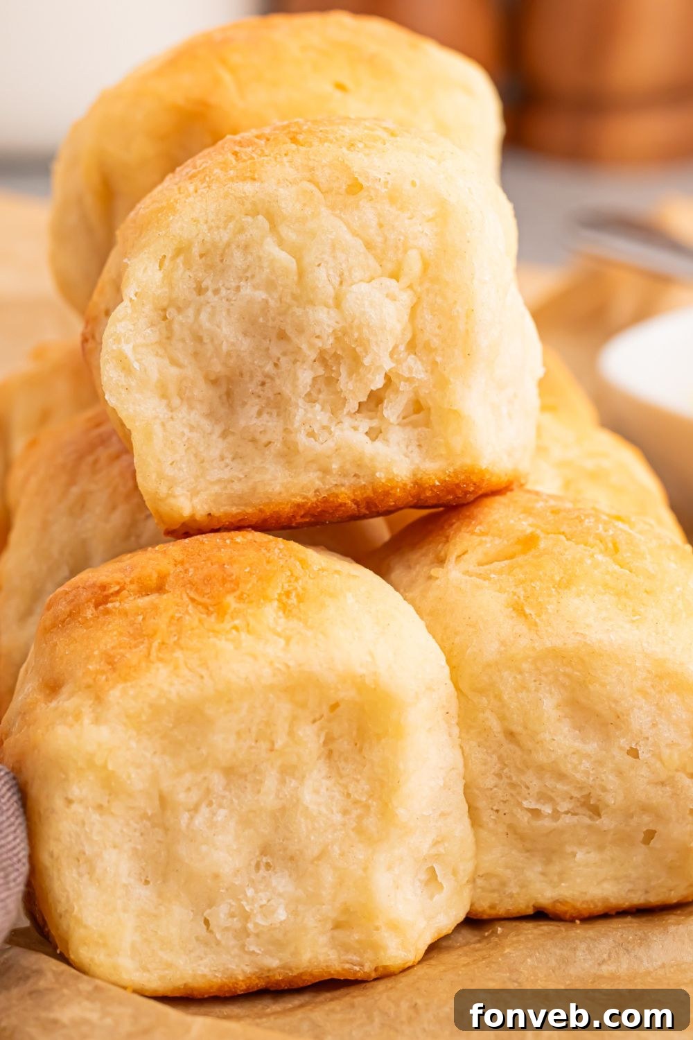 A stack of golden 2-Ingredient Dinner Rolls on a table, showcasing their soft, fluffy texture, with small dishes of salt and pepper blurred in the background, implying they are ready for seasoning.