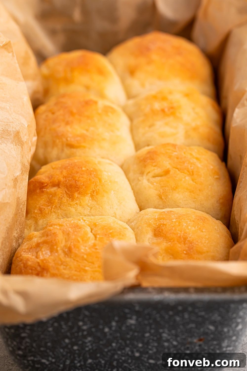 A baking tray filled with 2-Ingredient Dinner Rolls, lined with parchment paper, sitting on a wooden table, showcasing a freshly baked batch of these easy rolls.