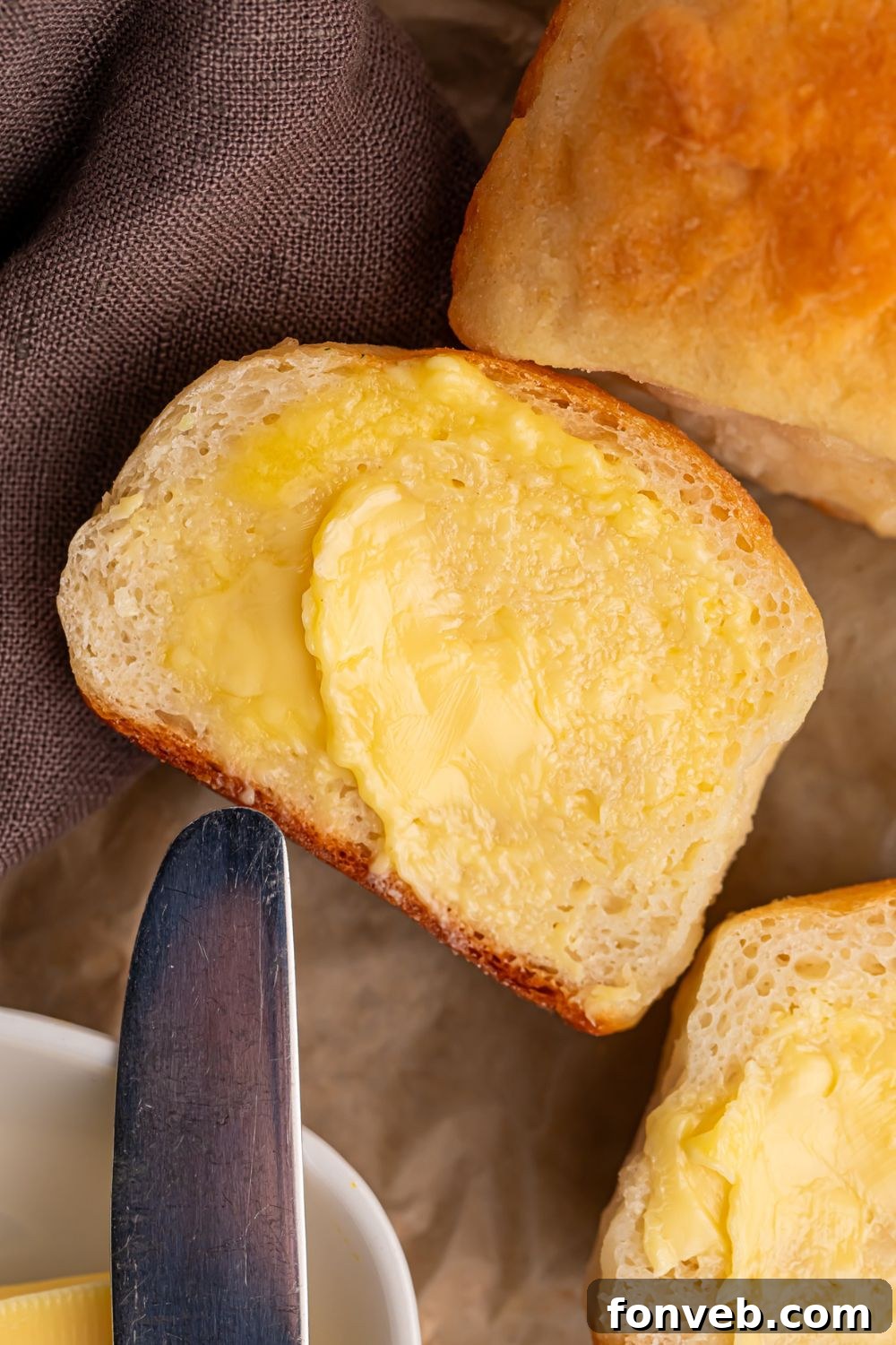 A close-up of a warm 2-Ingredient Dinner Roll split open and generously spread with melting butter, topped with fresh herbs, showcasing its soft interior and inviting aroma on a wooden table.