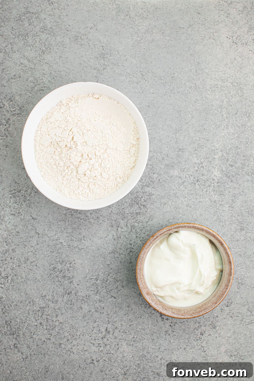Ingredients for 2-Ingredient Dinner Rolls: separate bowls of self-rising flour and plain Greek yogurt, neatly arranged on a table, ready for mixing.