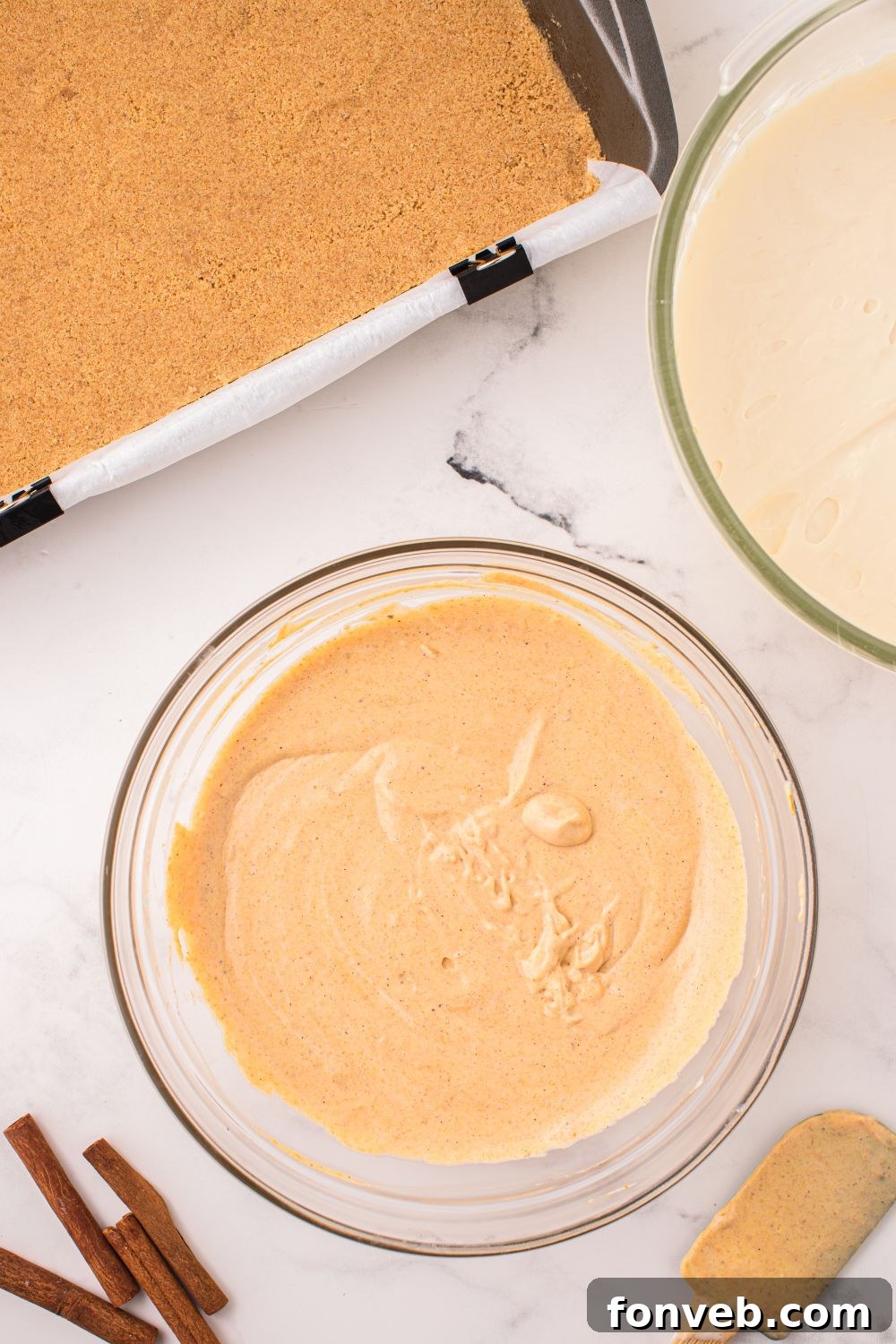 bowl of cheesecake batters and pan of graham cracker crumbs