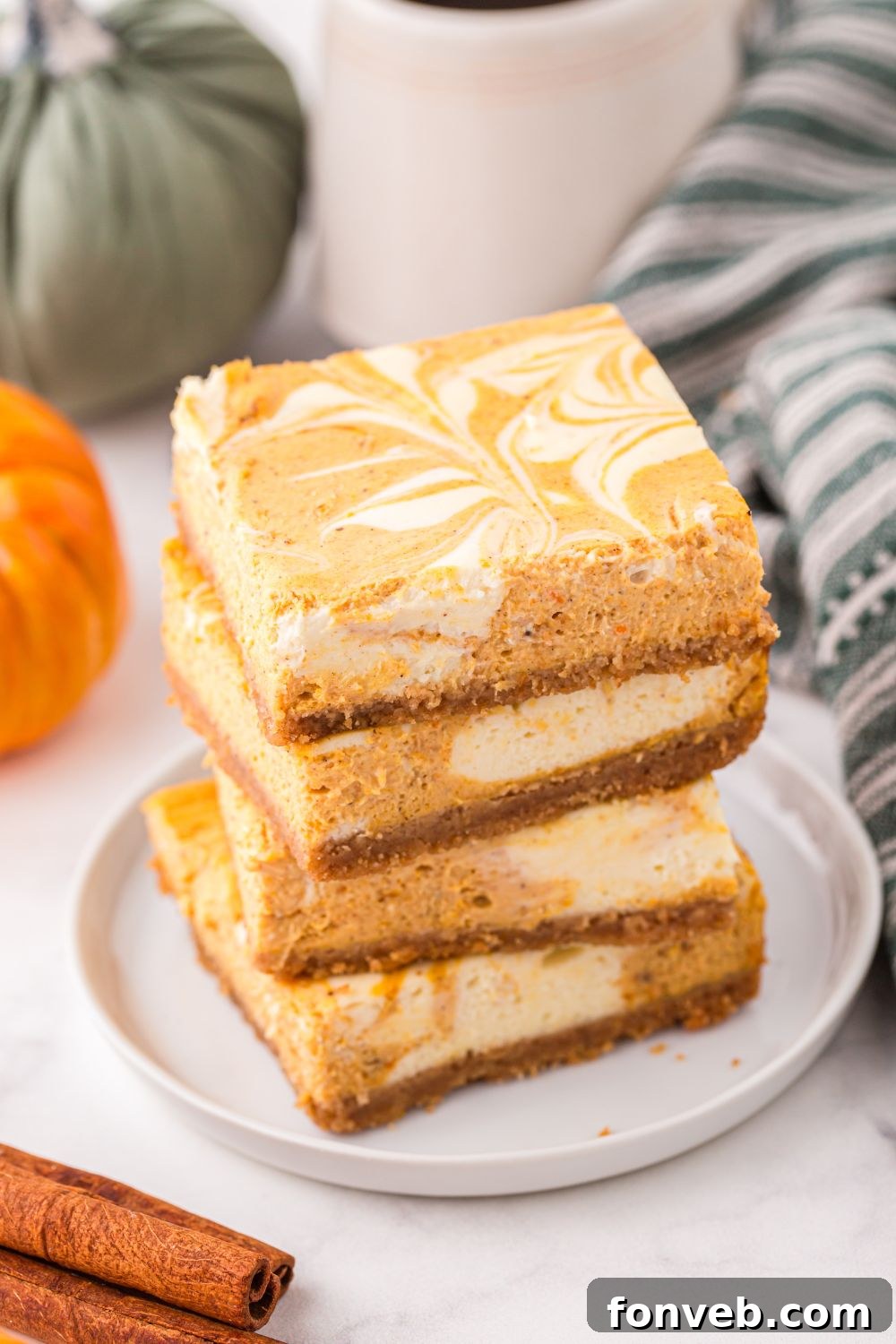 plate with a stack of Swirled Pumpkin Cheesecake Bars on it and coffee in a cup behind it