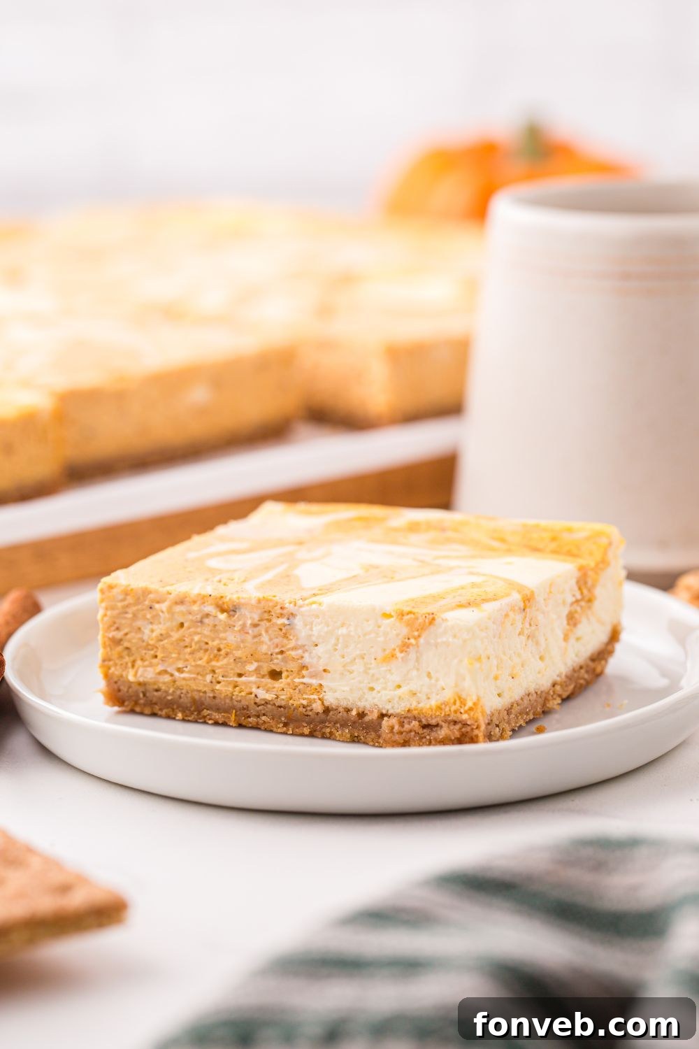 Swirled Pumpkin Cheesecake Bar on plate with the rest of bars behind it on table and a cup of coffee