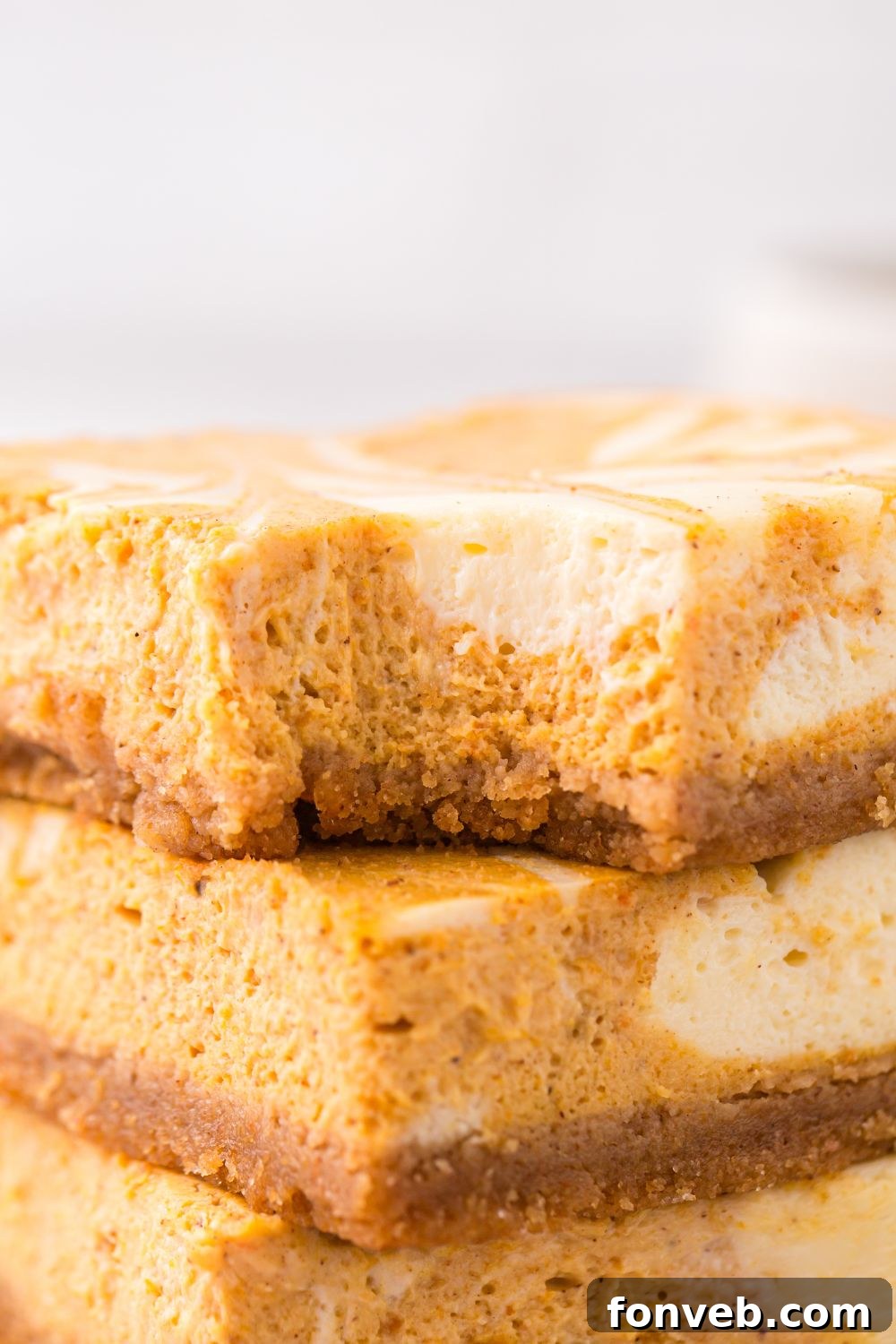 view of Swirled Pumpkin Cheesecake Bars stacked on top of one another with a bite taken out of top bar
