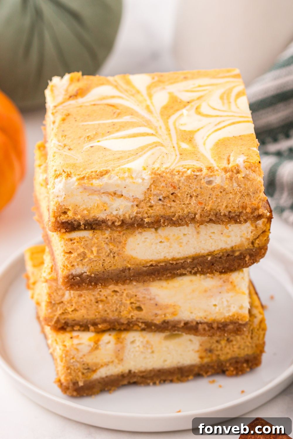 Swirled Pumpkin Cheesecake Bars stacked on a white plate sitting on a table decorated like fall 