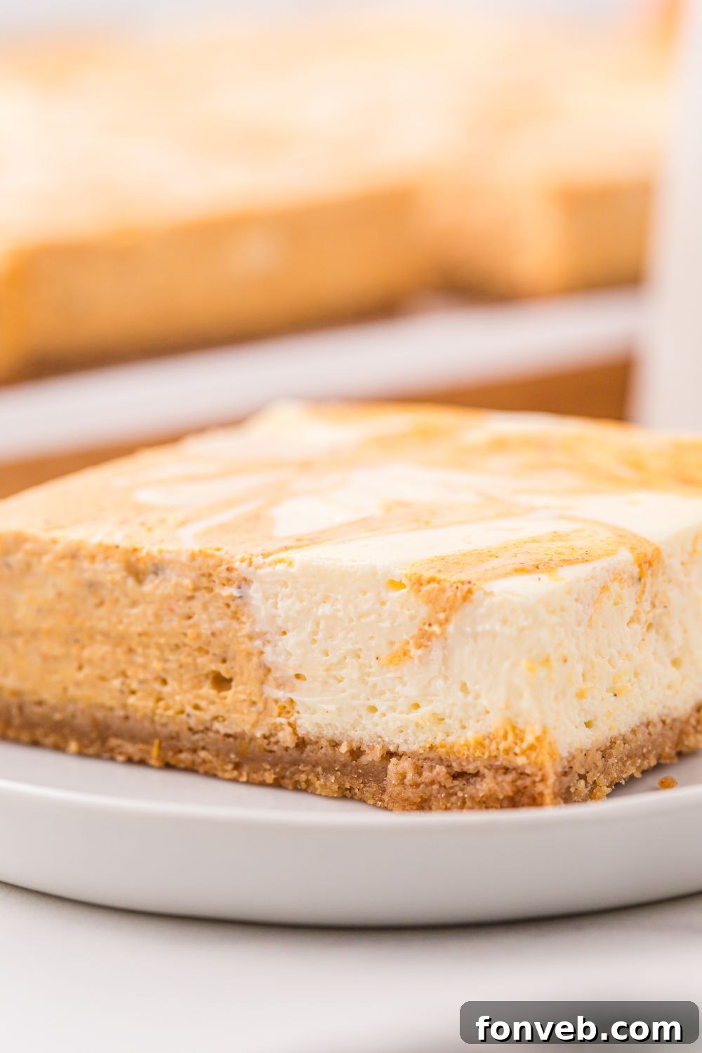 Swirled Pumpkin Cheesecake Bar on a plate with more bars behind it on table
