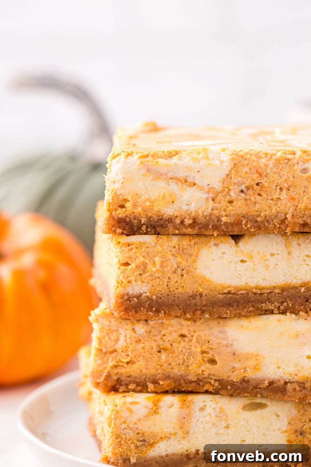 Swirled Pumpkin Cheesecake Bars stacked on table with pumpkin to side