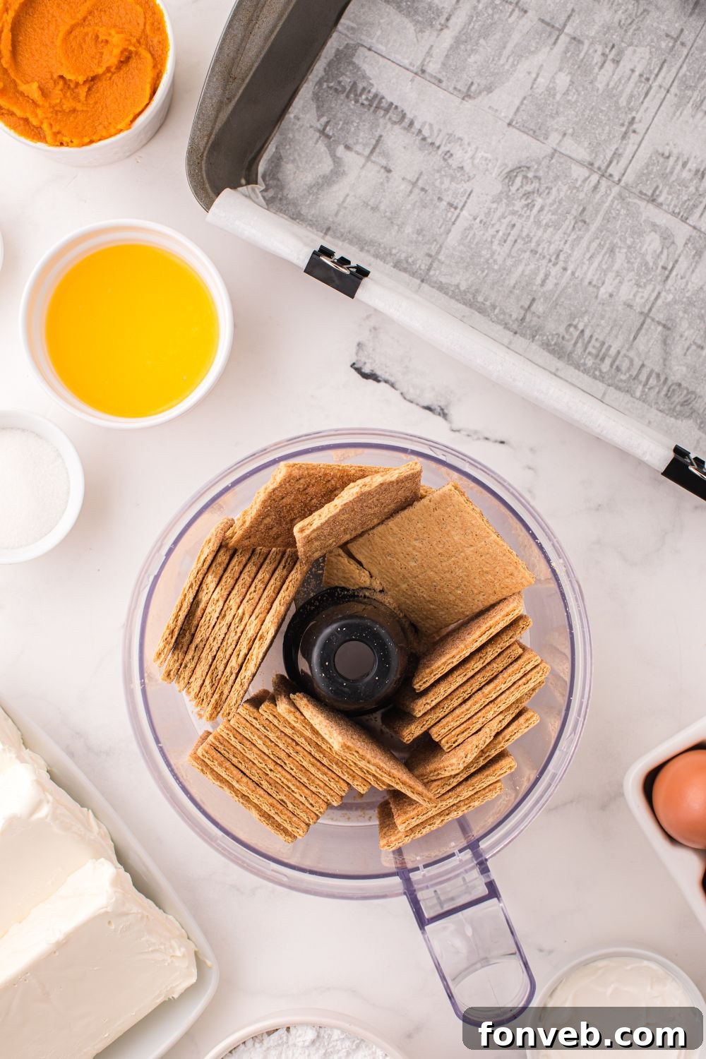 food processor with graham crackers and butter and sugar in small bowls to side for making Swirled Pumpkin Cheesecake Bars