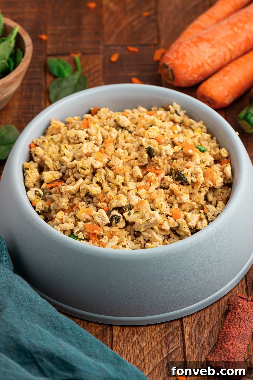 Homemade Turkey and Rice Dog Food with Veggies in a grey bowl on table with herbs and carrots behind bowl 