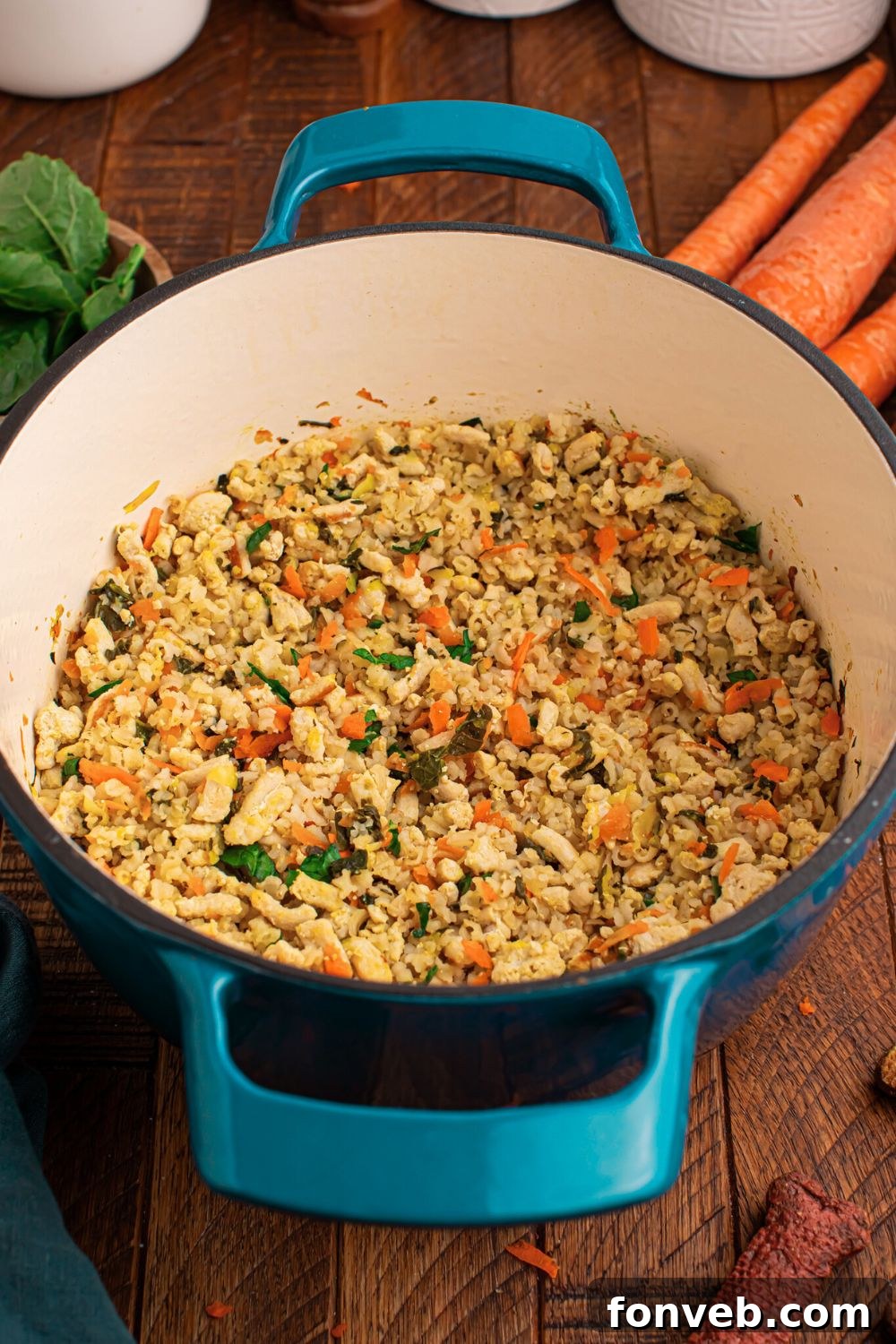 Homemade Turkey and Rice Dog Food with Veggies in a pot sitting on table with fresh herbs, carrots, and white containers behind pan on table 
