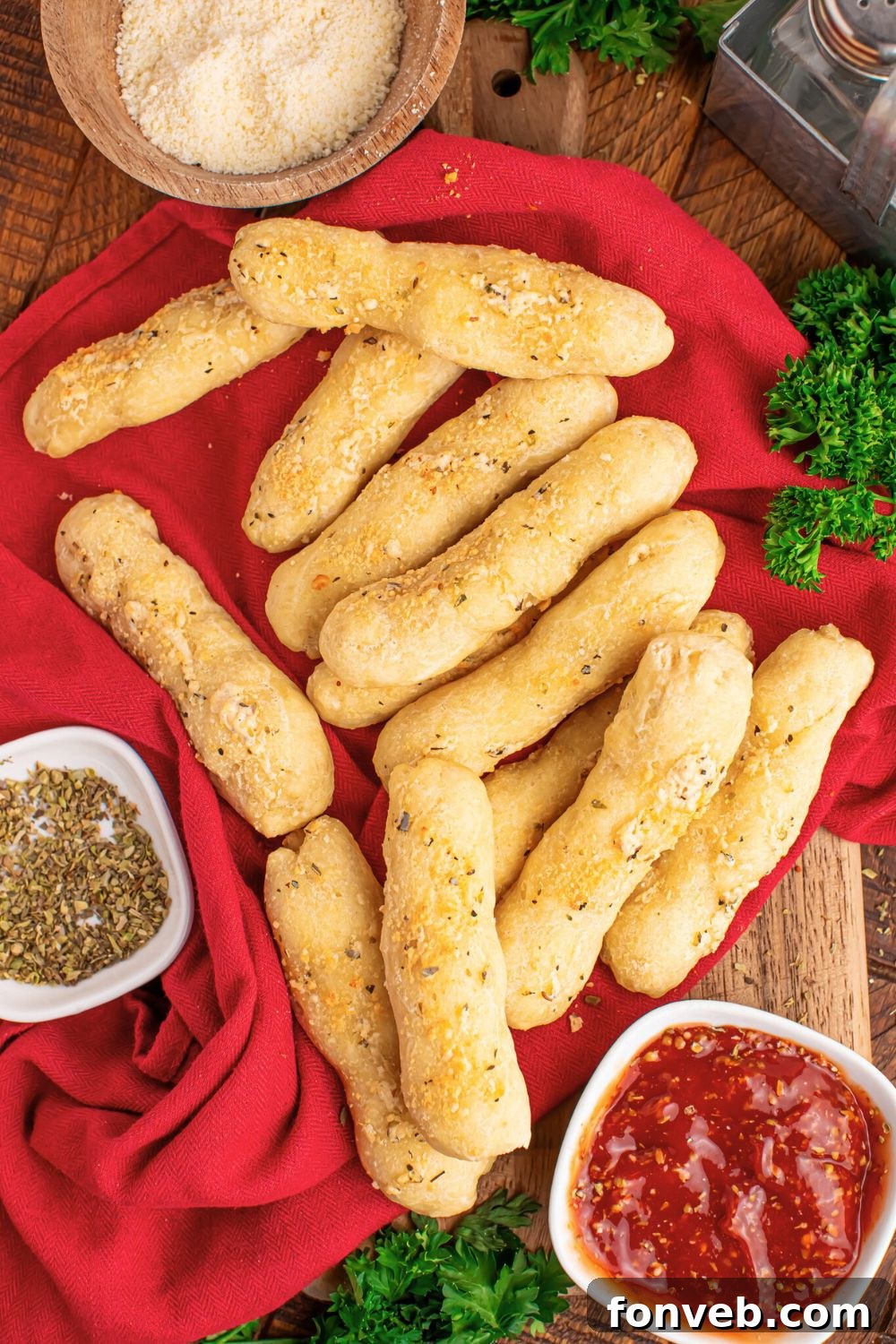 2-Ingredient Buttery Garlic Parmesan Breadsticks 3 2 ingredient breadsticks scattered on table with sauce in bowl and seasoning in another bowl