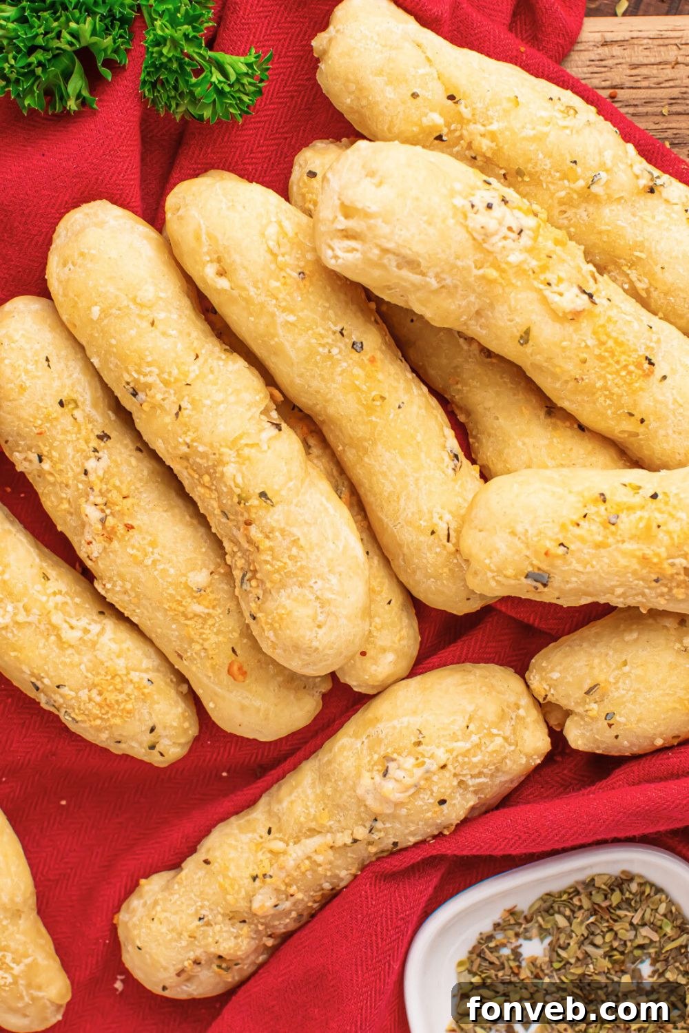 2-Ingredient Buttery Garlic Parmesan Breadsticks 22 red towel with a stack of 2 Ingredient Garlic Parmesan Breadsticks on top and a bit of parsley behind it on table