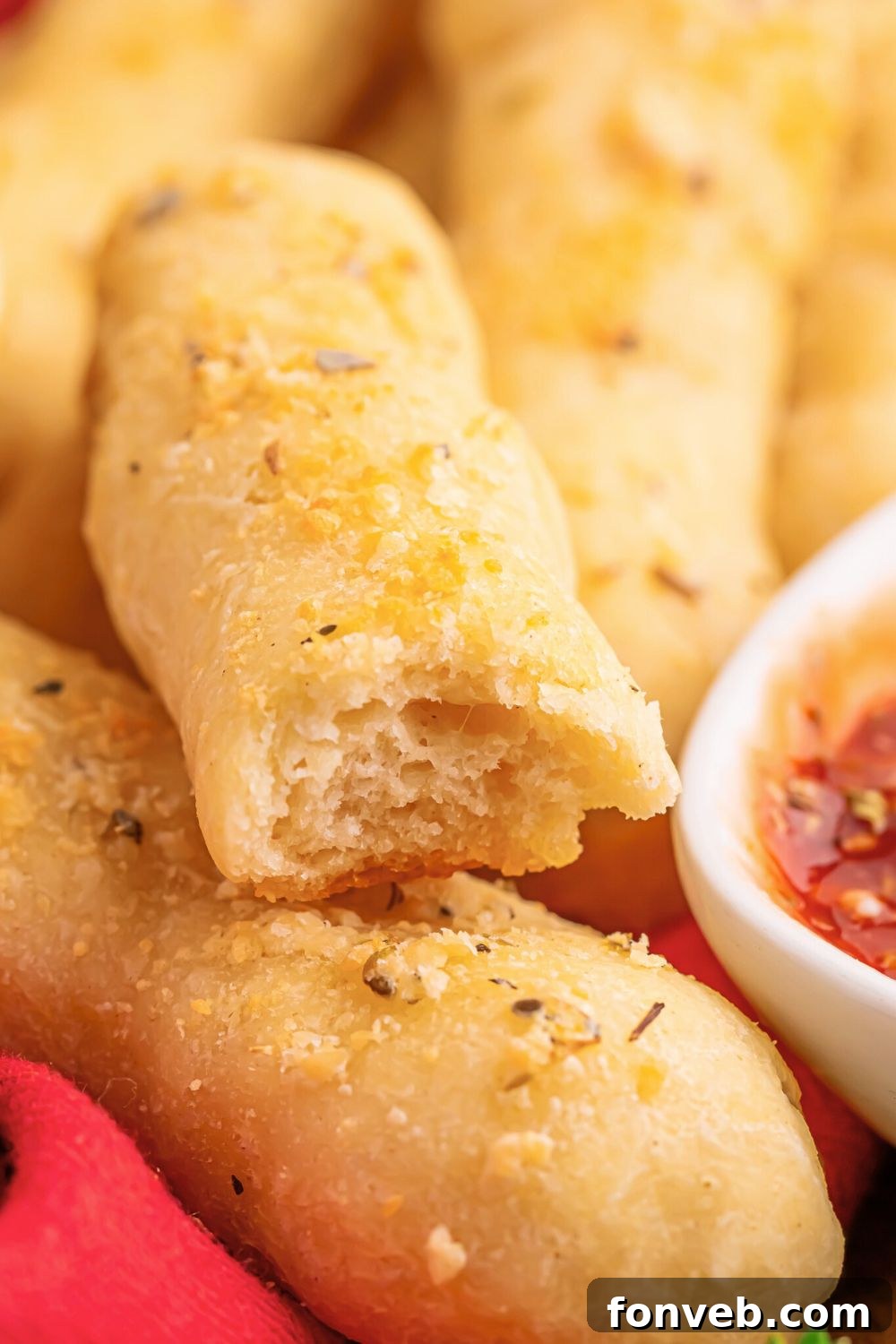 2-Ingredient Buttery Garlic Parmesan Breadsticks 4 2 ingredient breadsticks on table with one having a bite taken out of it and a bowl of sauce to side of breadsticks