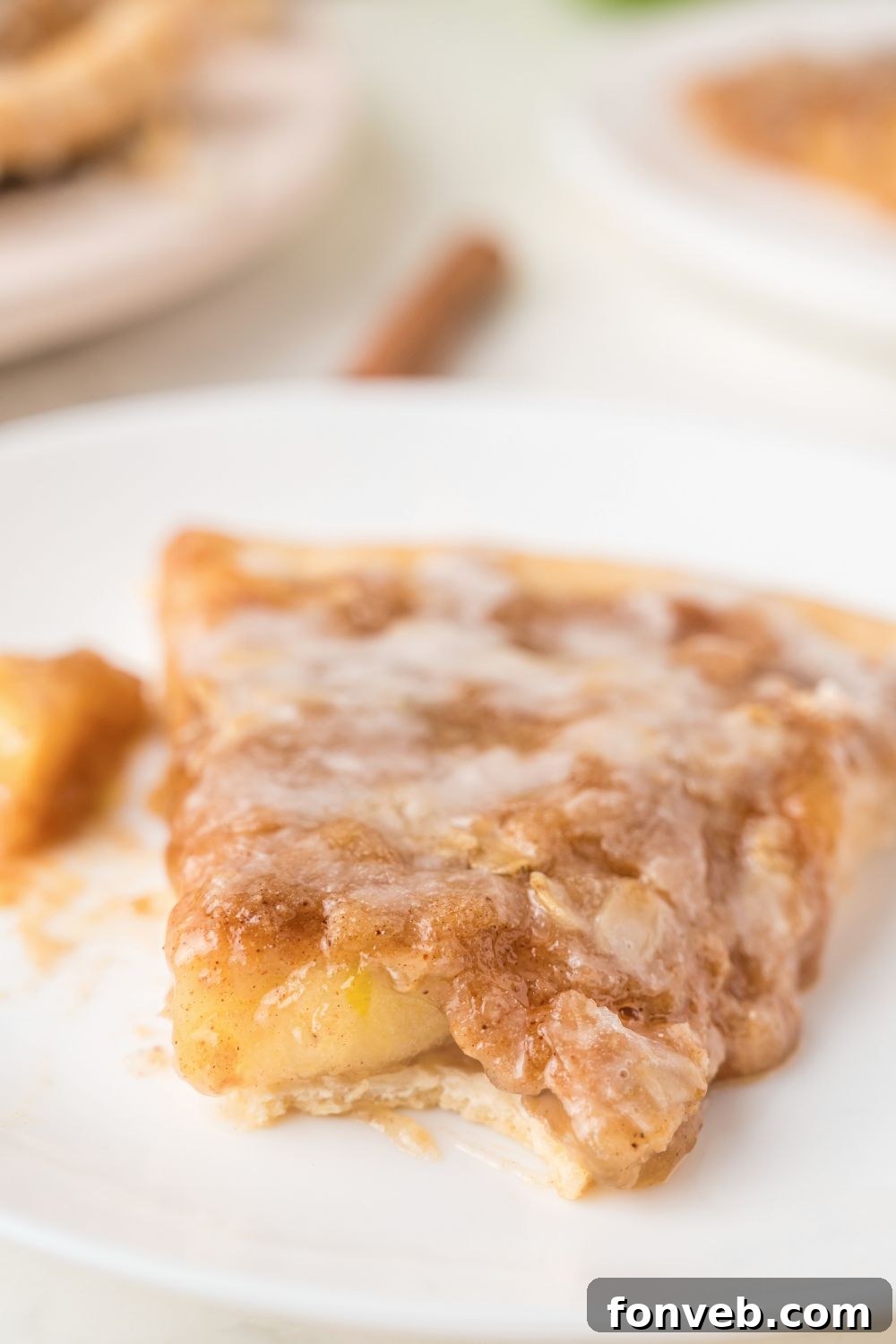 A delectable slice of Apple Pie Pizza on a white plate, with a bite taken out, revealing the layers of fruit, crumble, and soft crust.