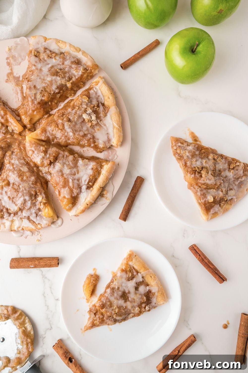 An overhead view of a beautifully styled table featuring an Apple Pie Pizza, individual plates with slices, and scattered cinnamon sticks, creating a cozy autumnal scene.