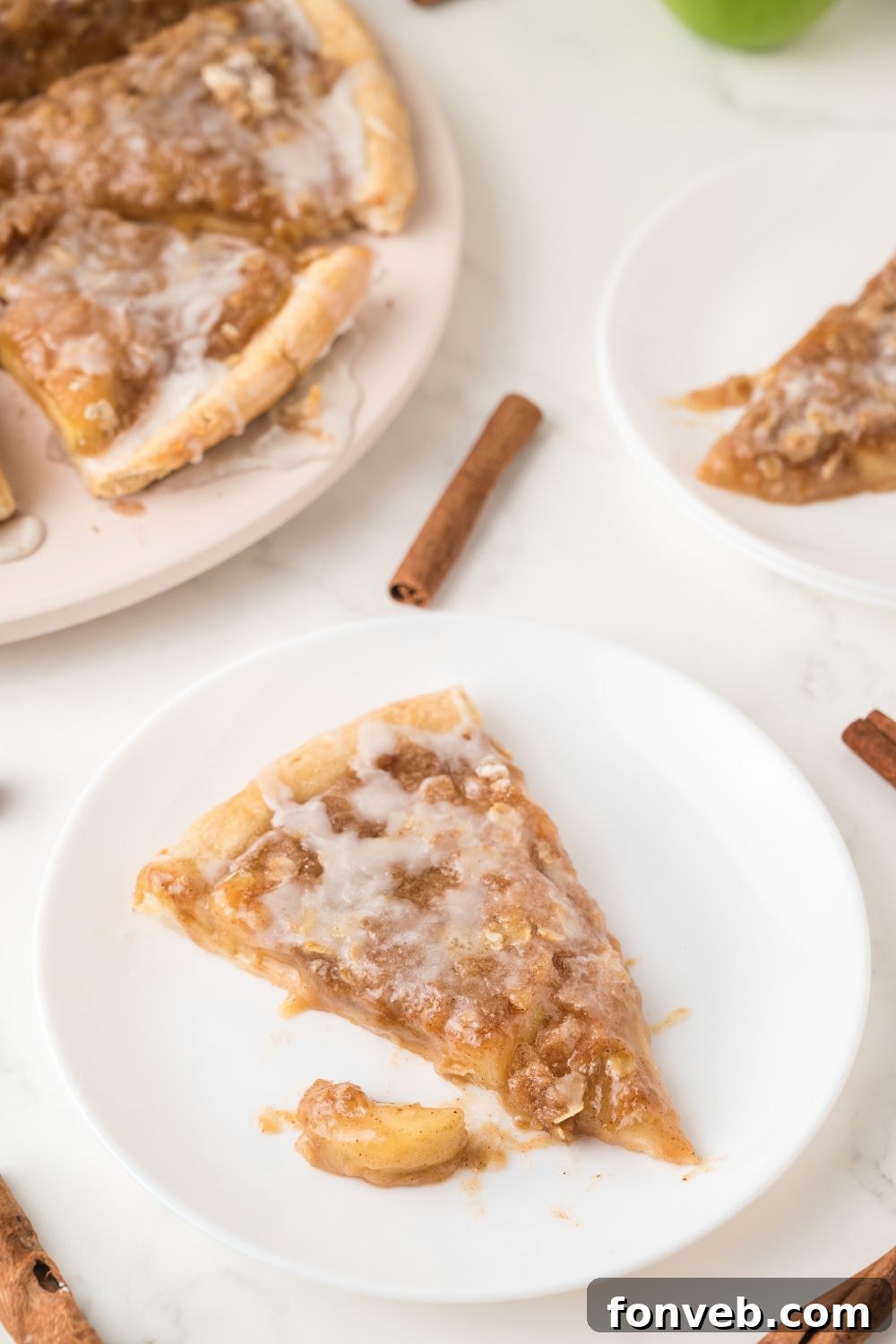 A slice of Apple Pie Pizza neatly arranged on a plate next to the main pizza on a wooden table, emphasizing its readiness for serving.