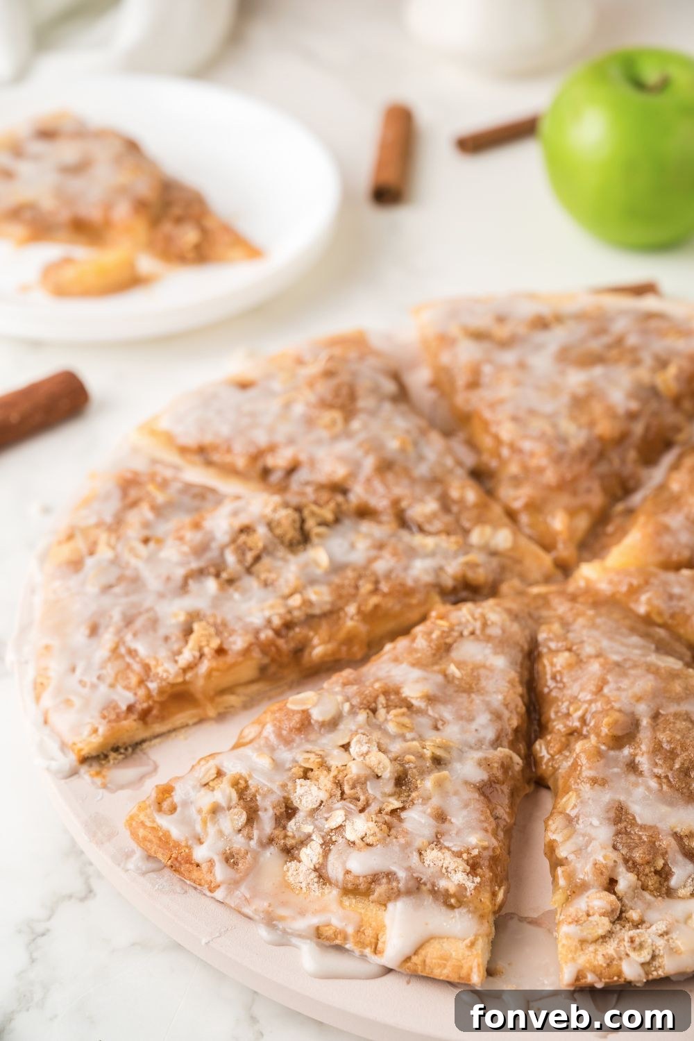 Sliced Apple Pie Pizza arranged circularly on a wooden table, with fresh apples and cinnamon sticks forming an attractive background.
