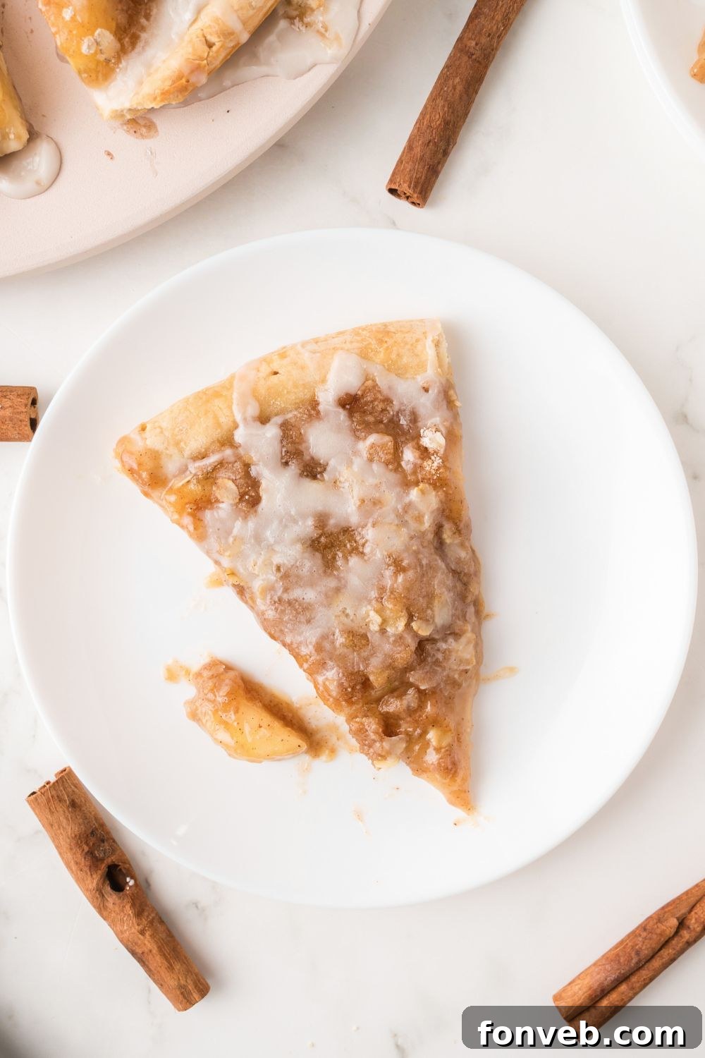 A sliced Apple Pie Pizza on a plate, surrounded by a few cinnamon sticks on a wooden table, highlighting its enticing aroma and presentation.
