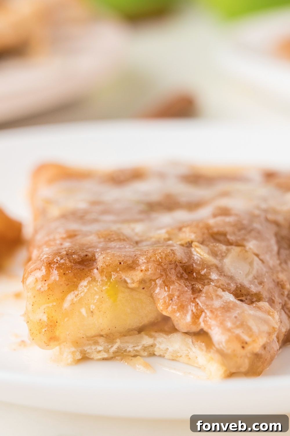A slice of Apple Pie Pizza on a plate with a noticeable bite taken out, highlighting the irresistible deliciousness of the dessert.