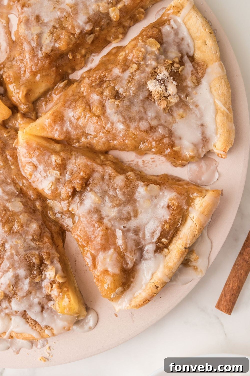 A wide overhead shot of an Apple Pie Pizza presented on a baking tray, surrounded by cinnamon sticks on a rustic table, inviting shared enjoyment.