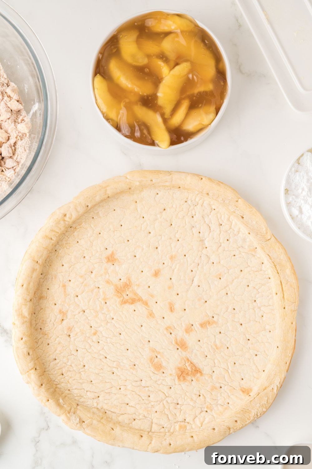 Individual ingredients for Apple Pie Pizza laid out on a table, including a pizza crust, a can of apple pie filling, oats, butter, sugar, and flour.
