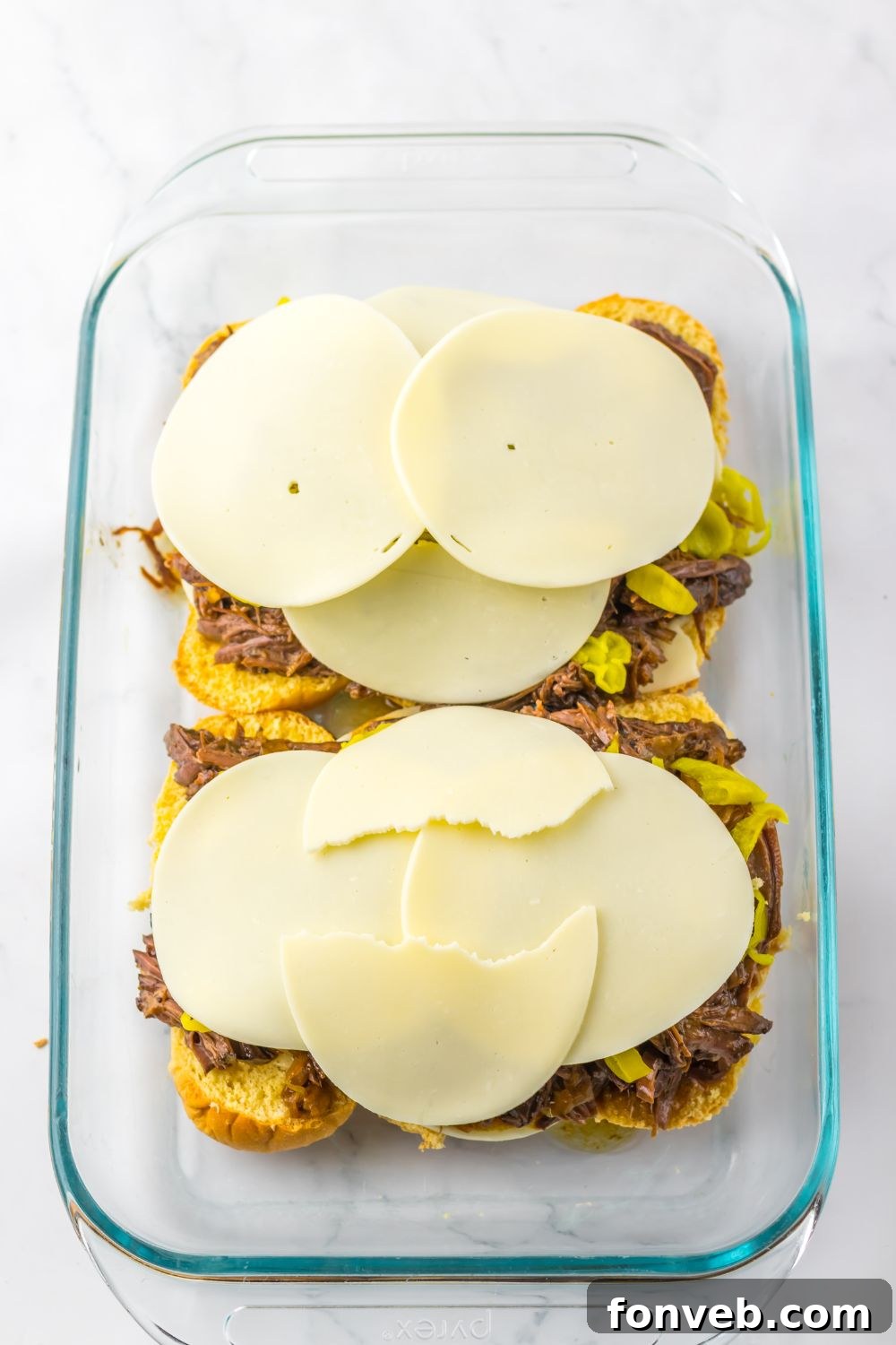 Deliciously Simple Slow Cooker Mississippi Pot Roast Sliders 11 provolone cheese on top of meat and peppers in a casserole pan