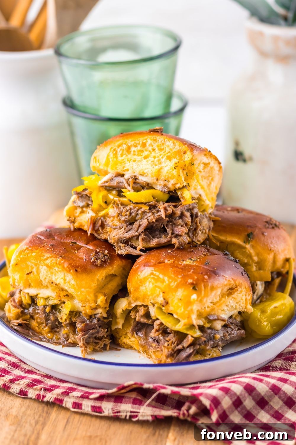 Deliciously Simple Slow Cooker Mississippi Pot Roast Sliders 13 Mississippi Pot Roast Sliders stacked on a plate with glasses behind the plate