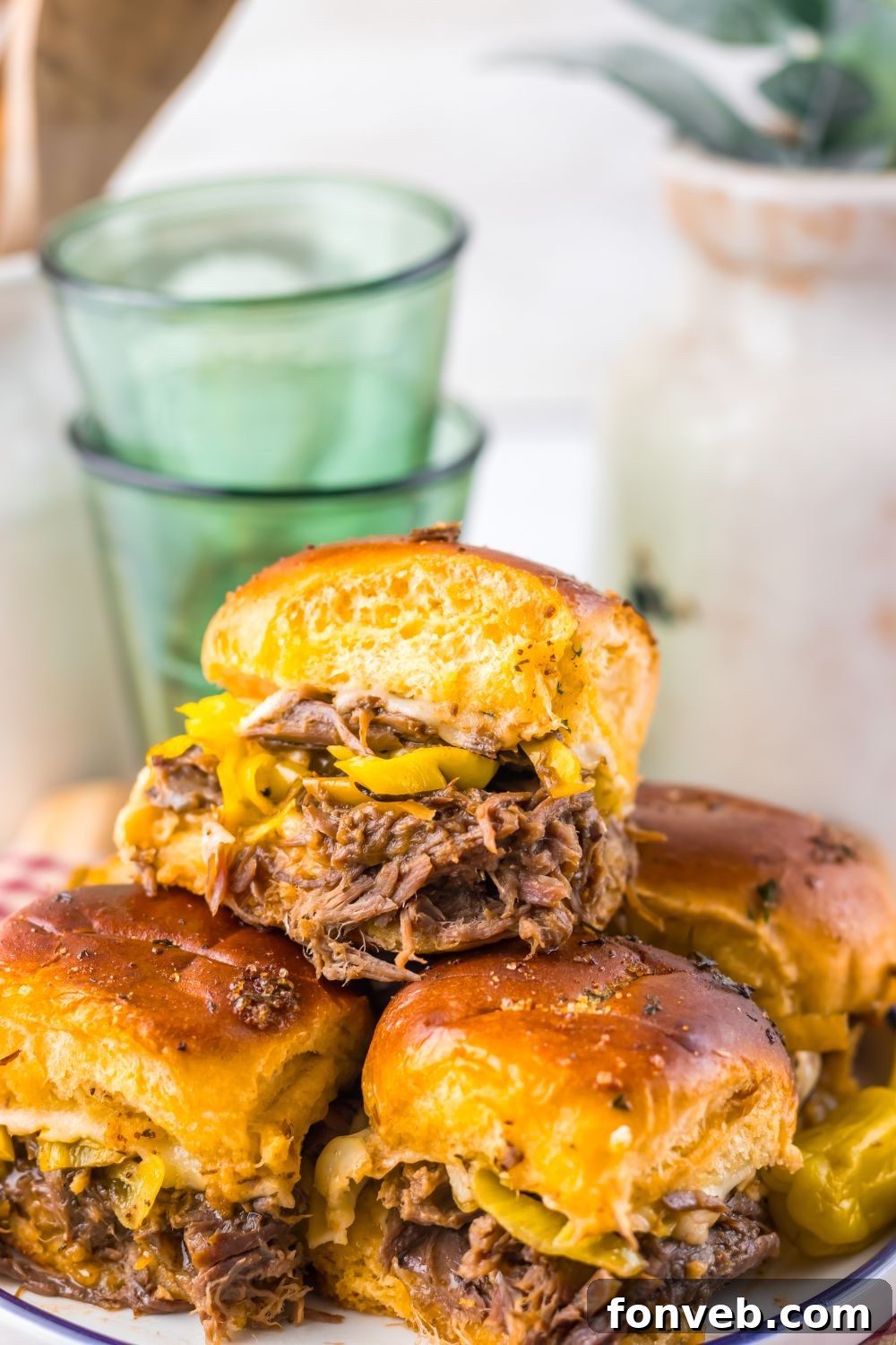 Deliciously Simple Slow Cooker Mississippi Pot Roast Sliders 14 Slow Cooker Mississippi Pot Roast Sliders stacked on a plate with a close up of sliders on table