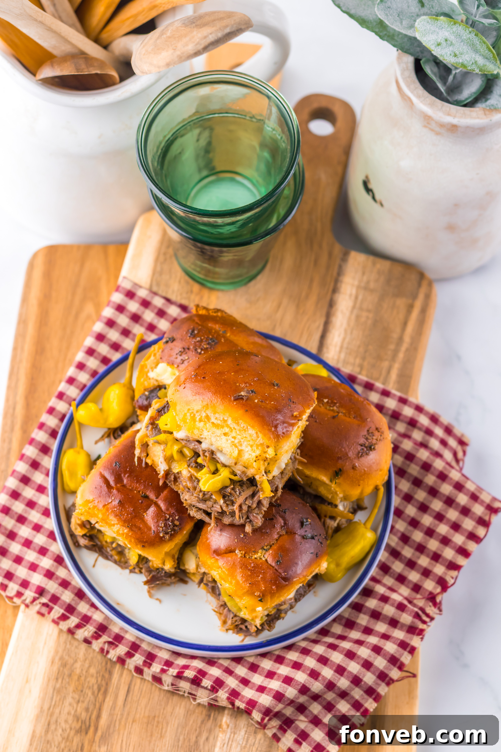 Deliciously Simple Slow Cooker Mississippi Pot Roast Sliders 16 Slow Cooker Mississippi Pot Roast Sliders on a plate with some dishes behind the plate full of burgers