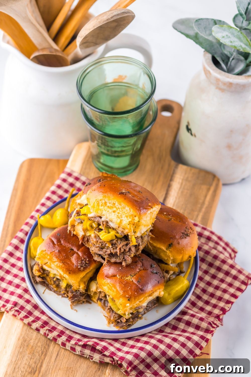 Deliciously Simple Slow Cooker Mississippi Pot Roast Sliders 18 Slow Cooker Mississippi Pot Roast Sliders on a table setting with glasses, cutting board and drink glasses behind it on table
