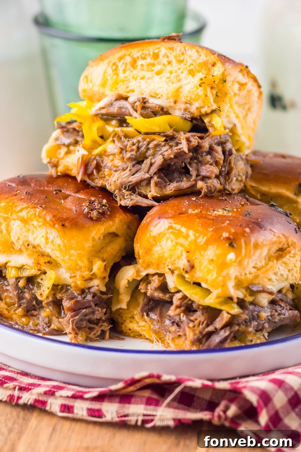 Deliciously Simple Slow Cooker Mississippi Pot Roast Sliders 19 close up of Slow Cooker Mississippi Pot Roast Sliders on a plate with a red checkered towel under it