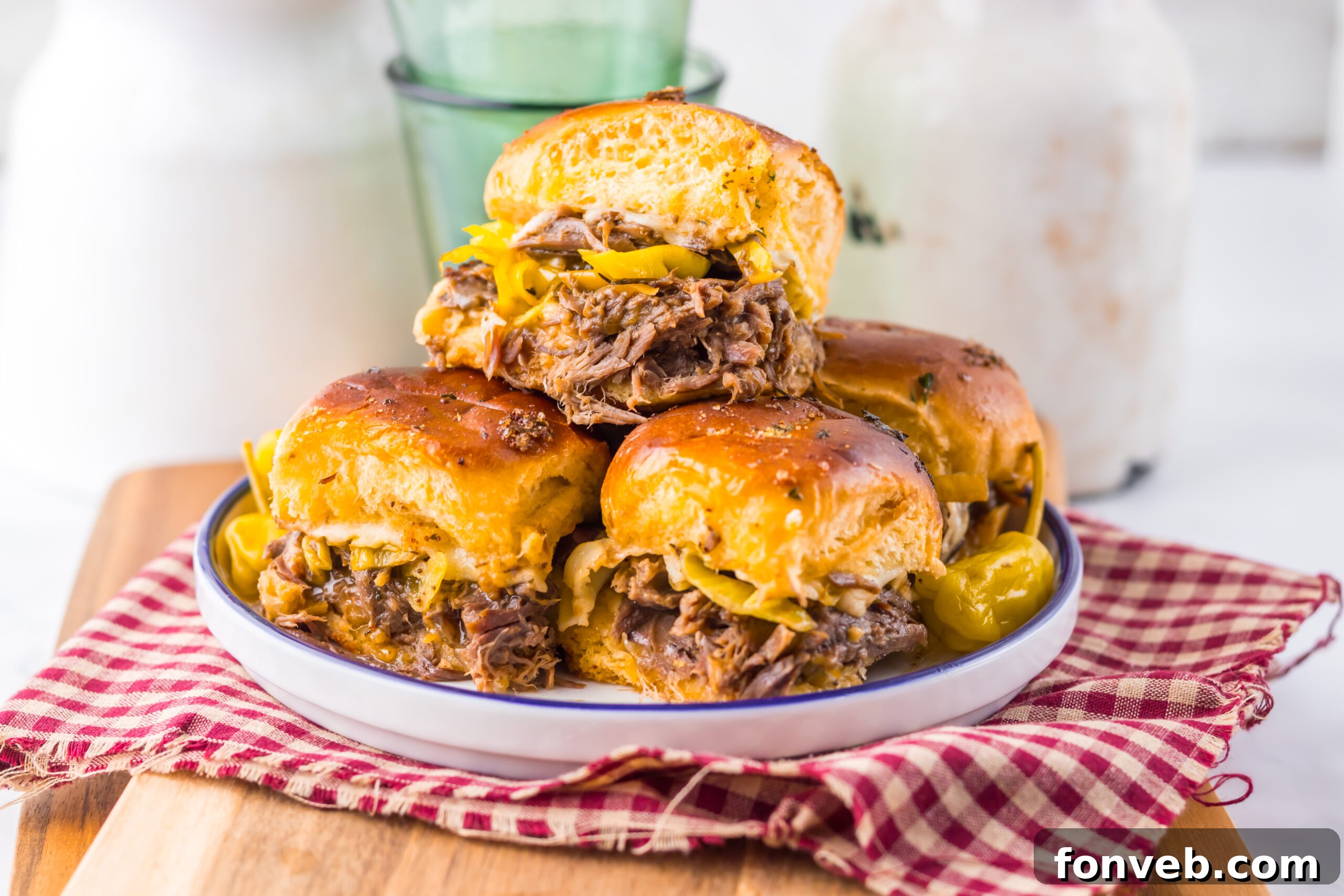 Deliciously Simple Slow Cooker Mississippi Pot Roast Sliders 20 close up of Slow Cooker Mississippi Pot Roast Sliders on a plate with a red checkered towel under it