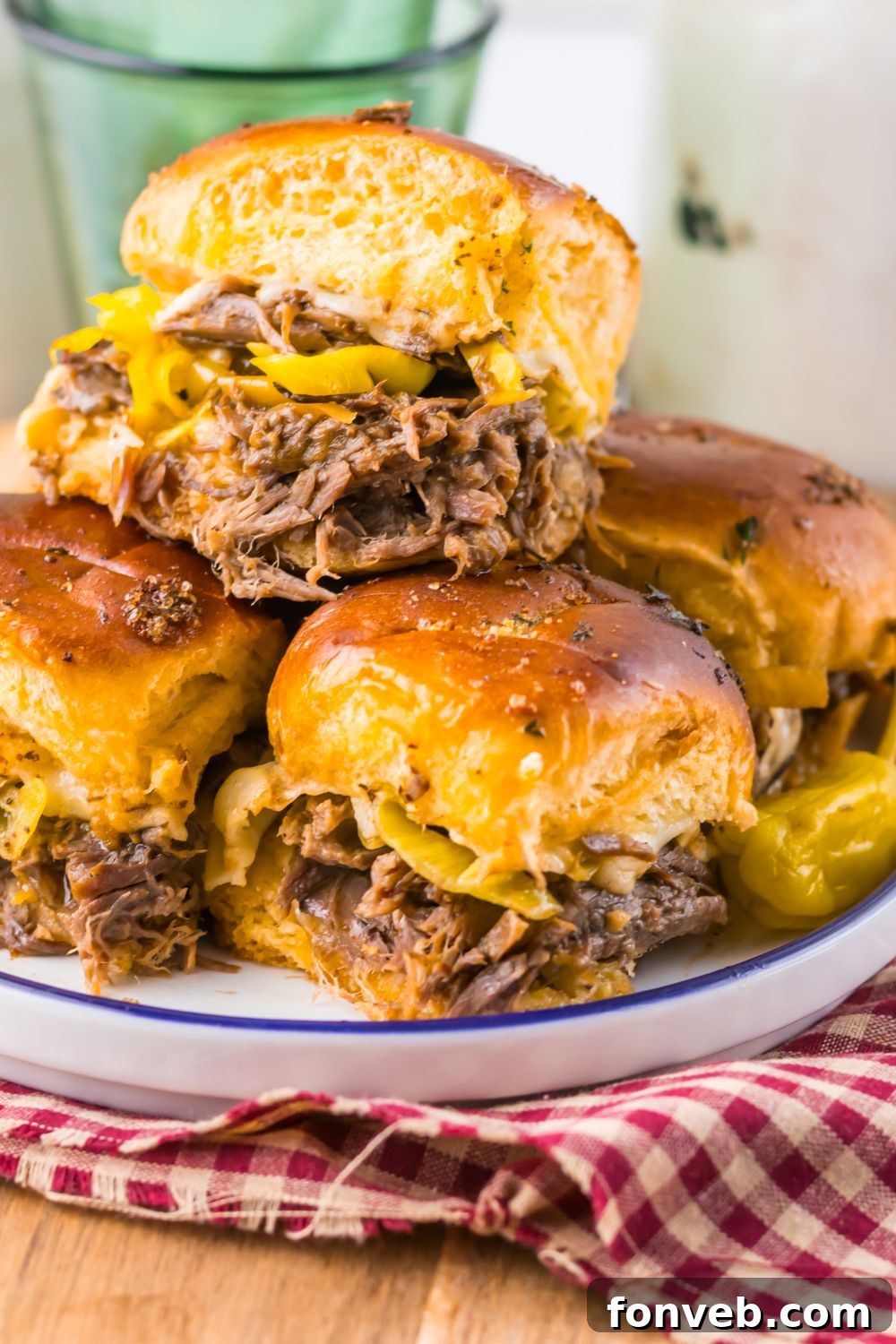 Deliciously Simple Slow Cooker Mississippi Pot Roast Sliders 3 Slow Cooker Mississippi Pot Roast Sliders stacked on plate with a red checkered towel under the plate