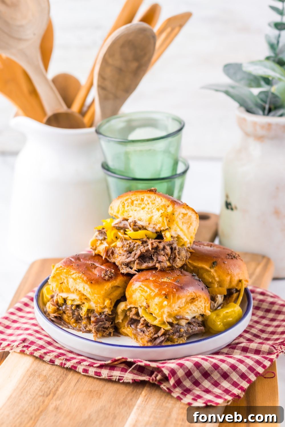 Deliciously Simple Slow Cooker Mississippi Pot Roast Sliders 4 Slow Cooker Mississippi Pot Roast Sliders on a plate with drinks behind it and a jar full of wooden kitchen utensils
